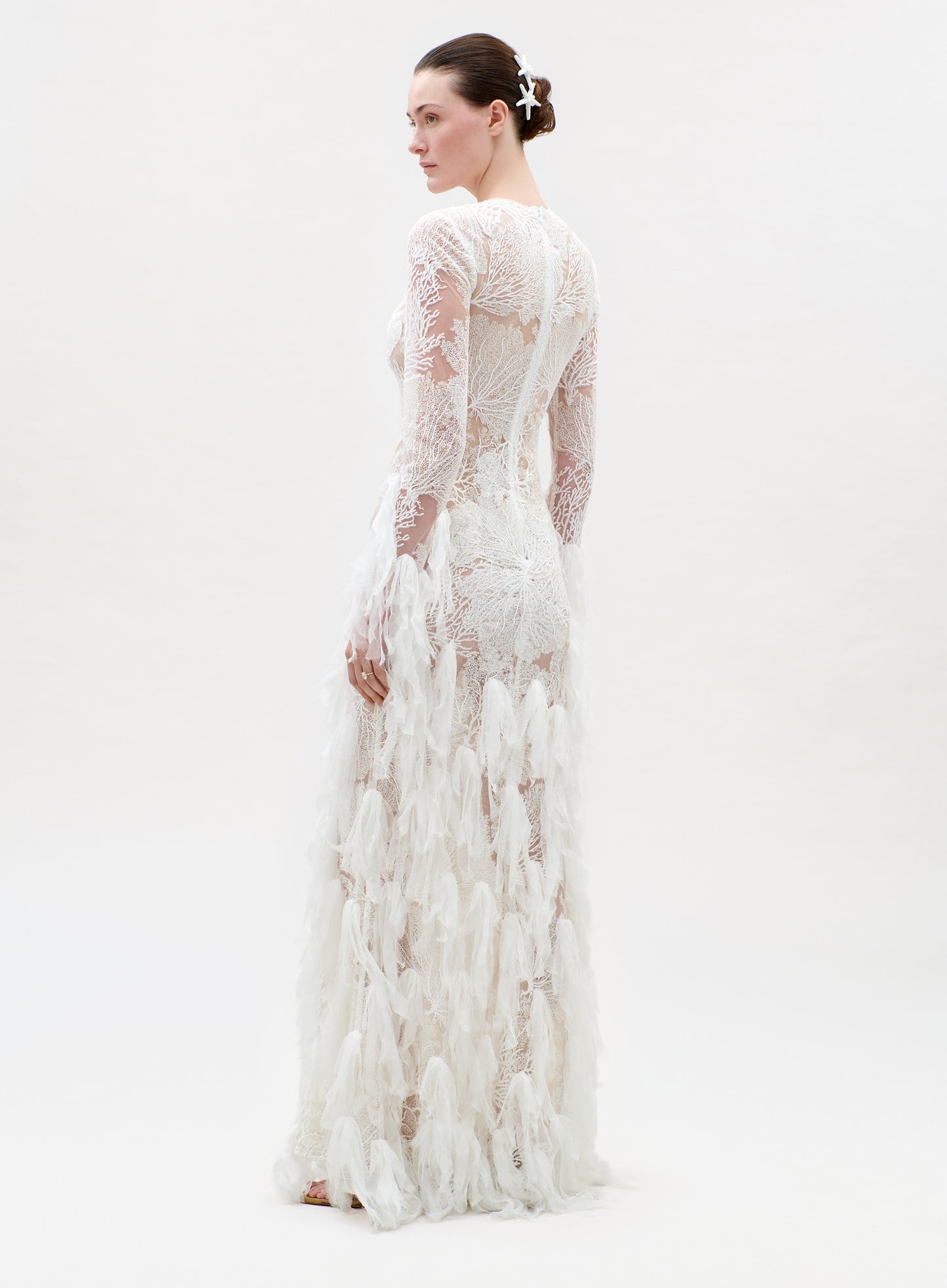 Woman wearing a long, white lace dress on a plain background
