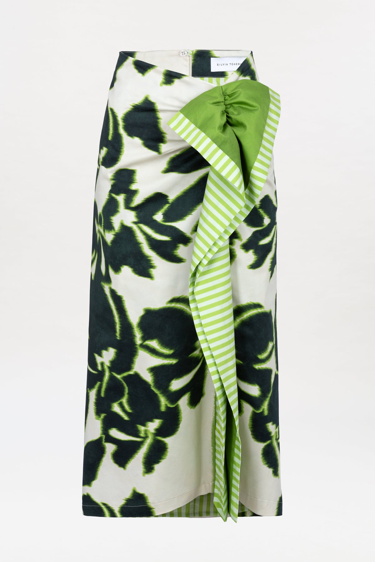 The Luana Skirt is a long skirt with a black and green floral print, featuring a green and white striped ruffle detail and a solid green accent bow at the waist.