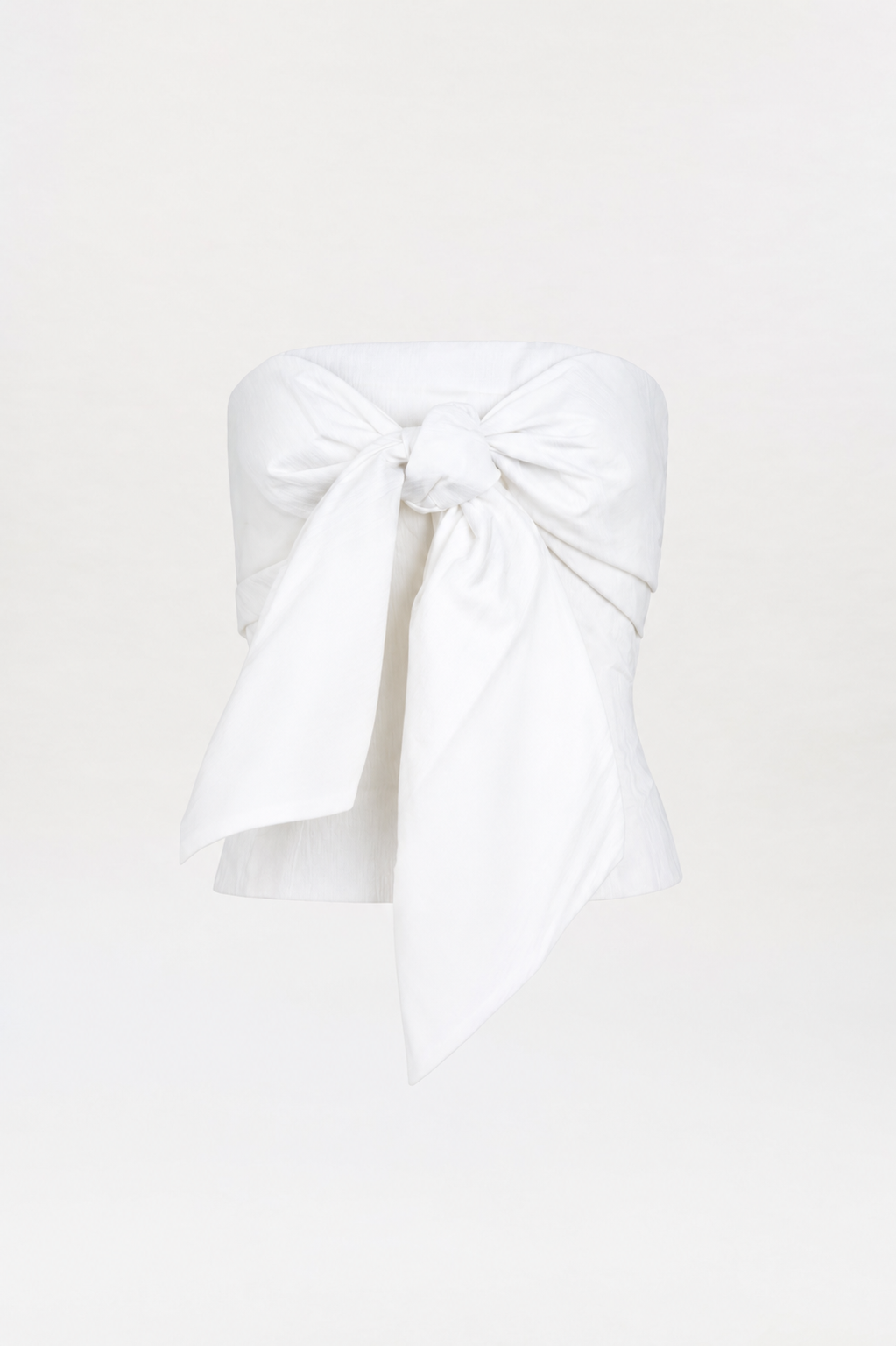 The Kacy Top is a strapless white top featuring a large, prominent bow tied at the bust, displayed on a plain white background.