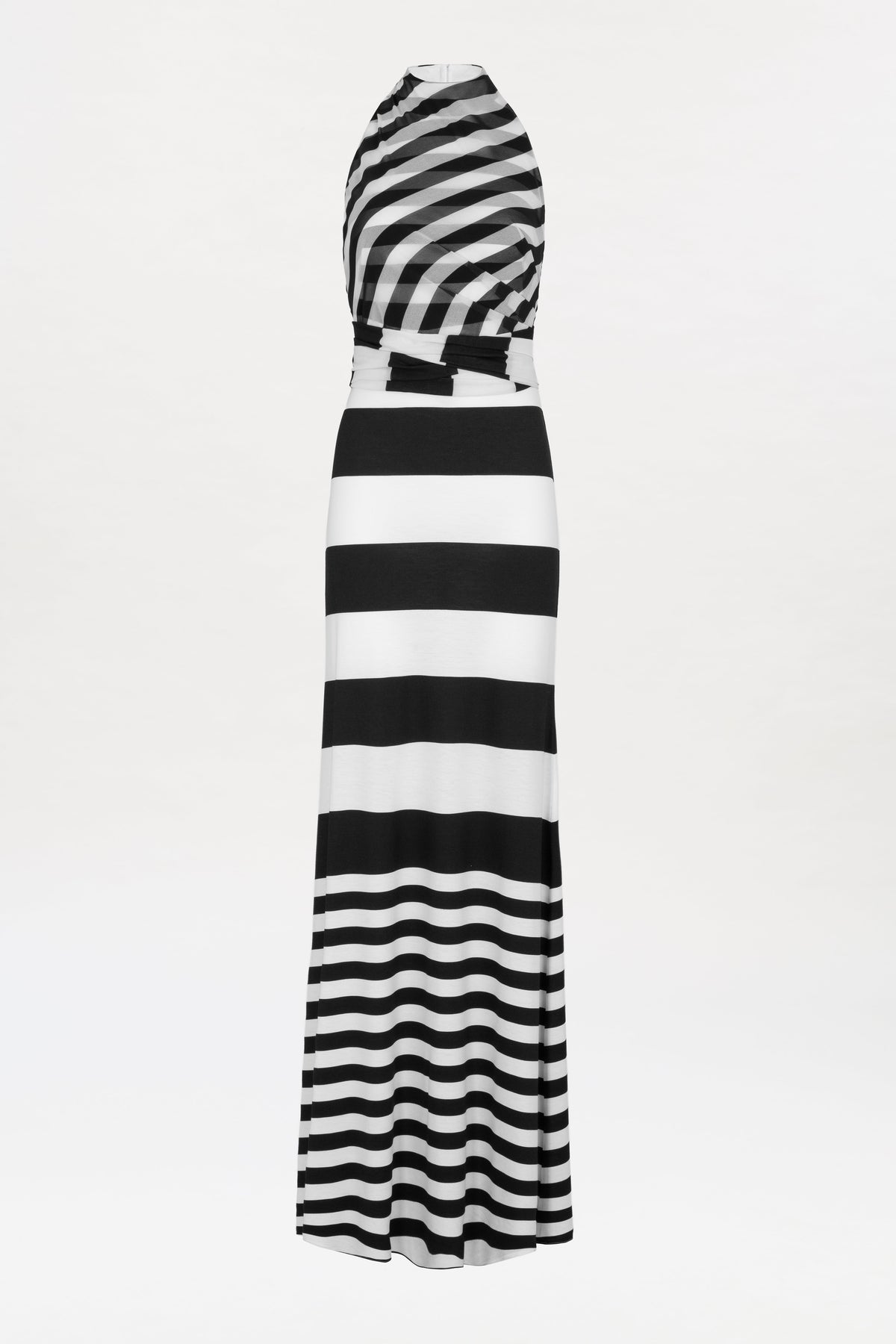 The Tove Dress is a sleeveless, floor-length design featuring black and white horizontal stripes of varying thickness. The top showcases diagonal stripes, while the skirt alternates thick and thin stripes, all set against a plain white background.