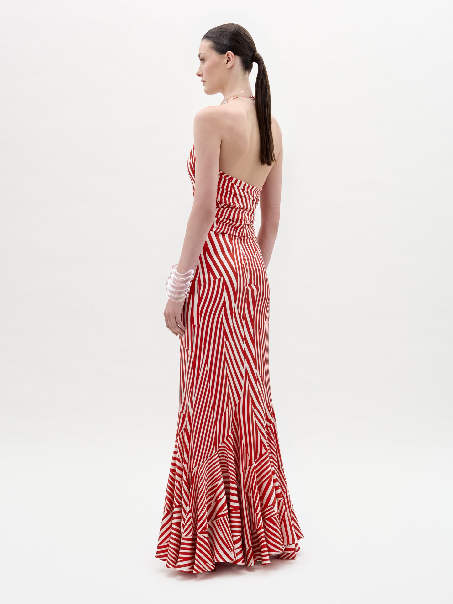 A woman with a ponytail wears the Florina Skirt—red and white striped, floor-length with a mermaid silhouette. She stands sideways, facing left, against a plain white background.