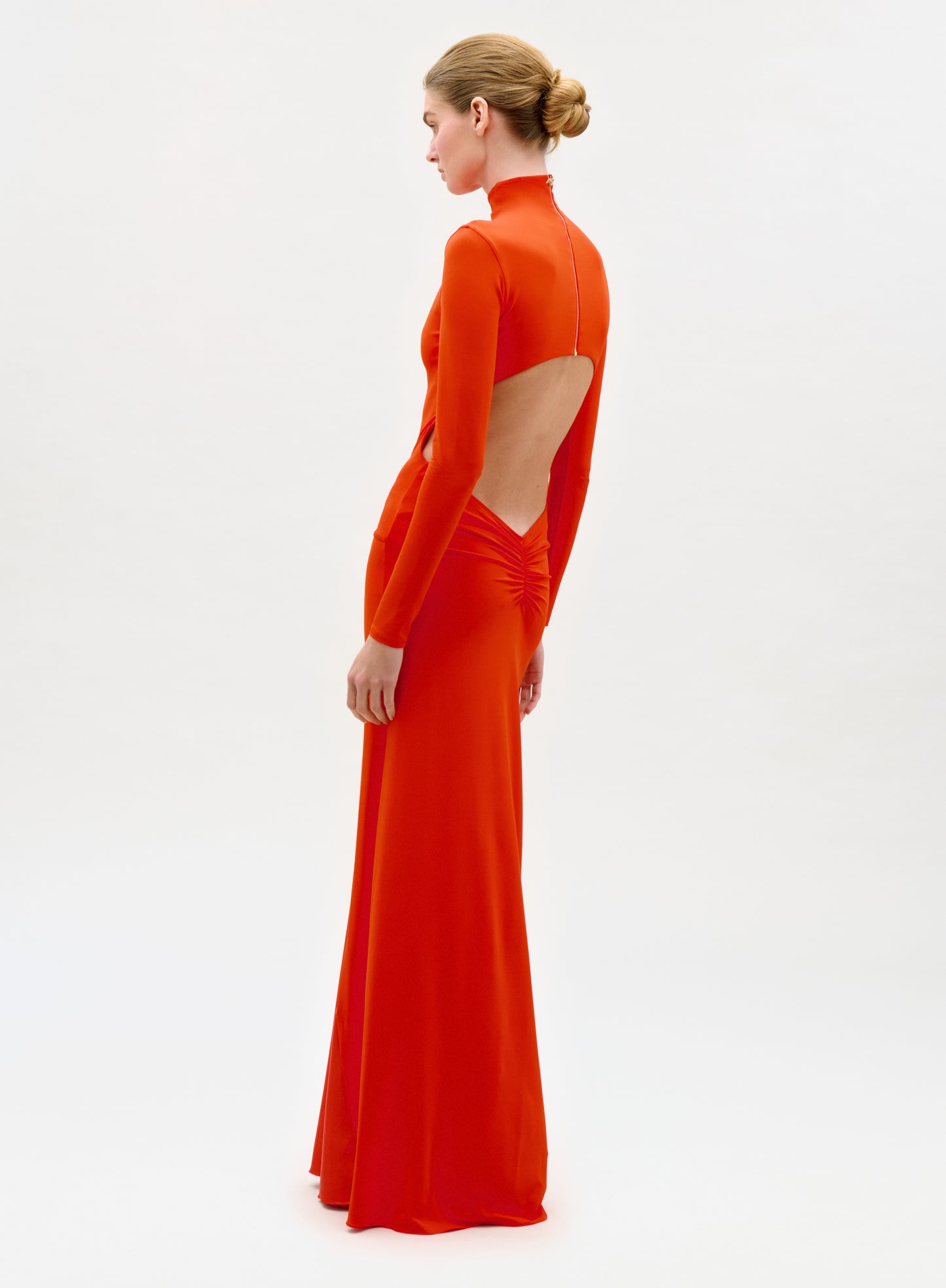 Woman wearing a bright orange long-sleeve gown with cut-out design on a white background