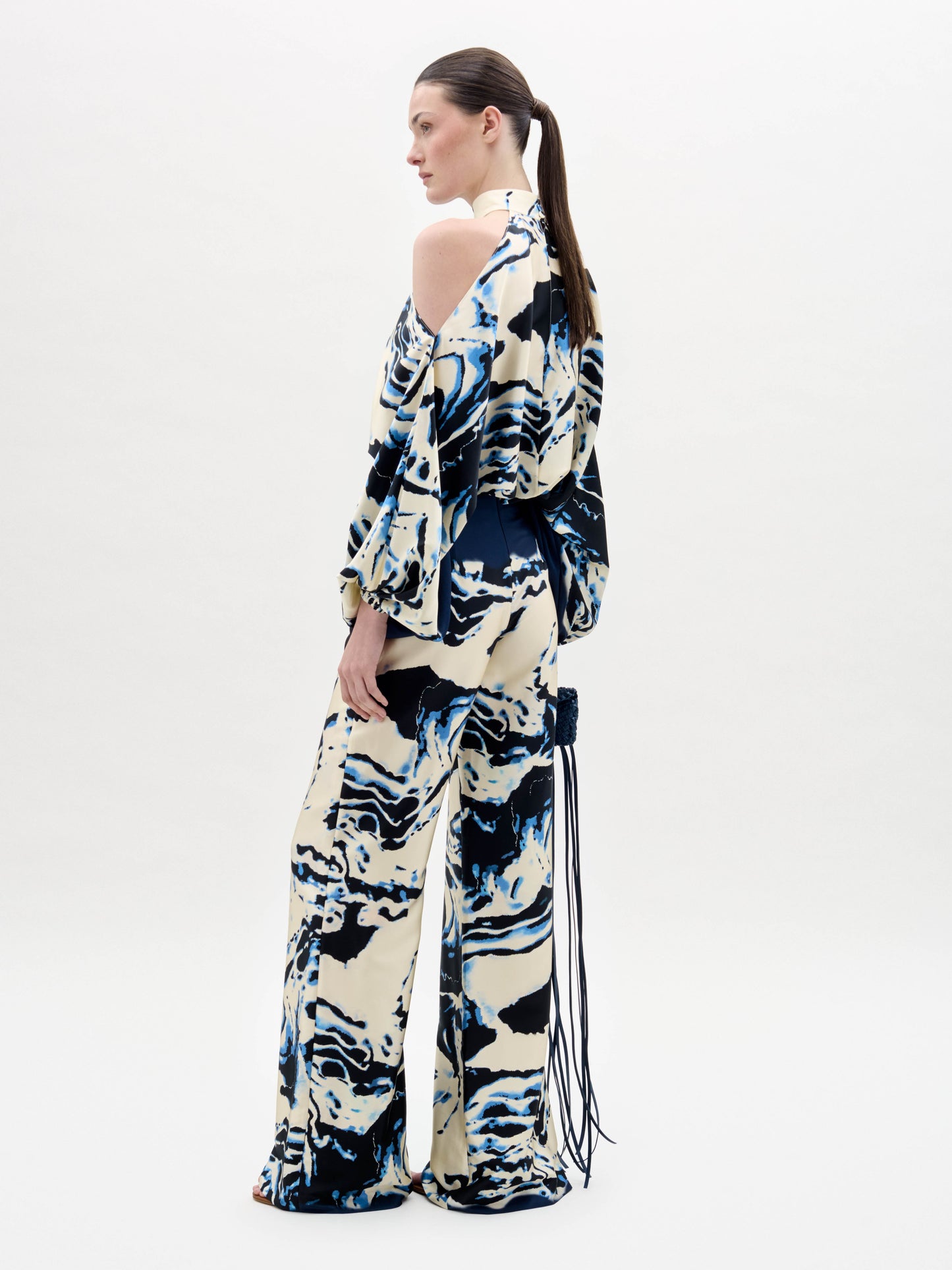 A woman stands against a plain white background wearing a cream and navy blue marble-patterned halter top with matching Como Pants in a wide-leg style.