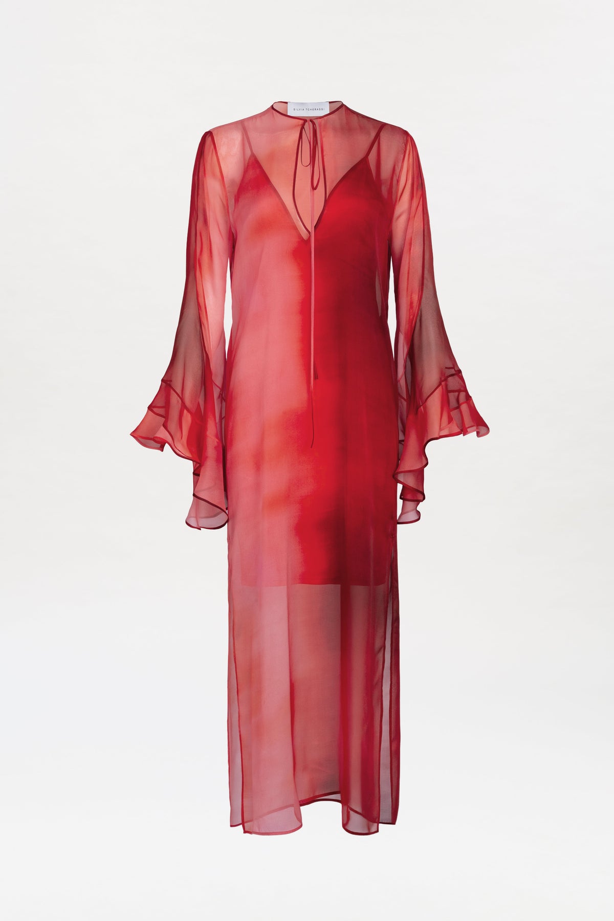 The Aries Dress features a sheer red, long-sleeve design with ruffled cuffs, a tie neckline, and a flowing ankle-length silhouette, showcased on a plain white background.