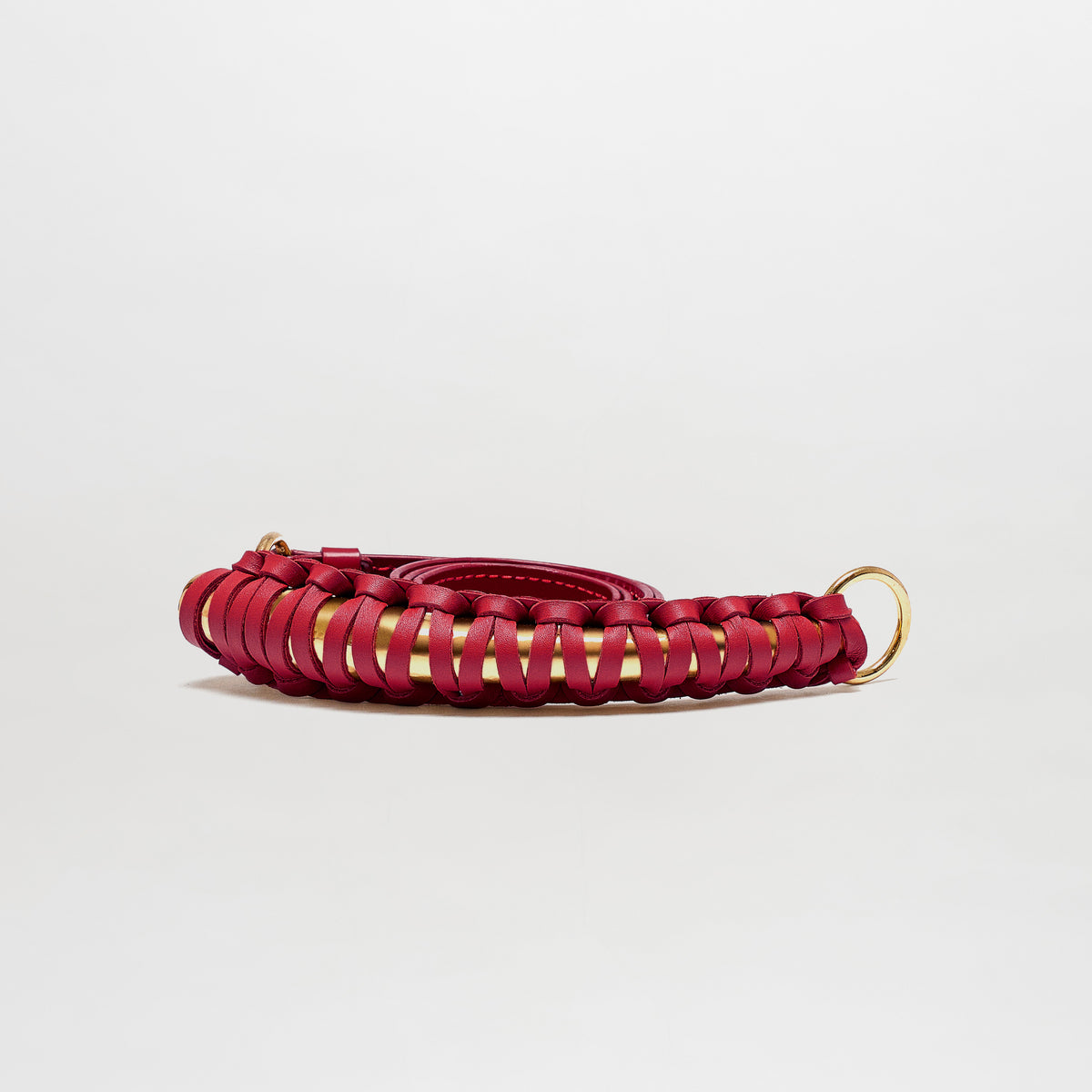 The Ife Belt, a coiled red leather accessory featuring gold rings at each end and made in Colombia, is displayed on a plain white background.
