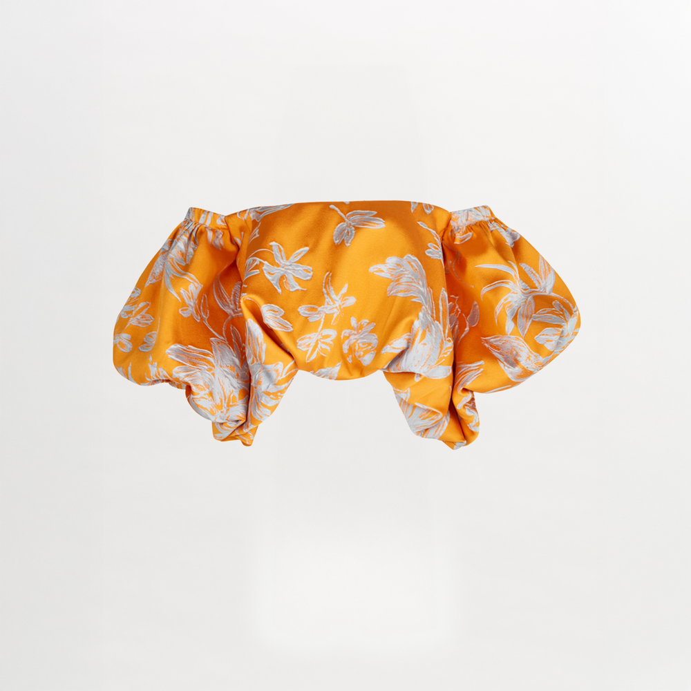 The Arezzo Blouse Apricot Silver showcases a charming orange off-the-shoulder design with a white floral pattern and voluminous sleeves, exuding polished elegance against a plain background.