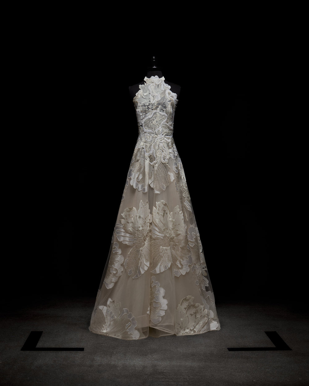 A person wearing the elegant, sleeveless Becca Dress, a white floral gown with a high neckline and sheer gloves, standing against a plain background.