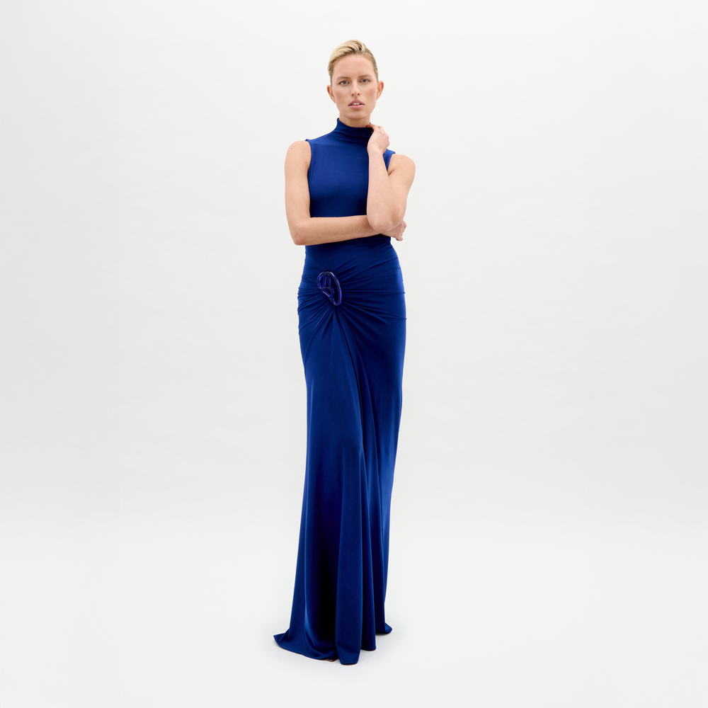 A woman poses against a plain white background, wearing the Bogna Dress—a sleeveless, high-neck maxi crafted from luxurious Italian fabric with elegant waist draping.