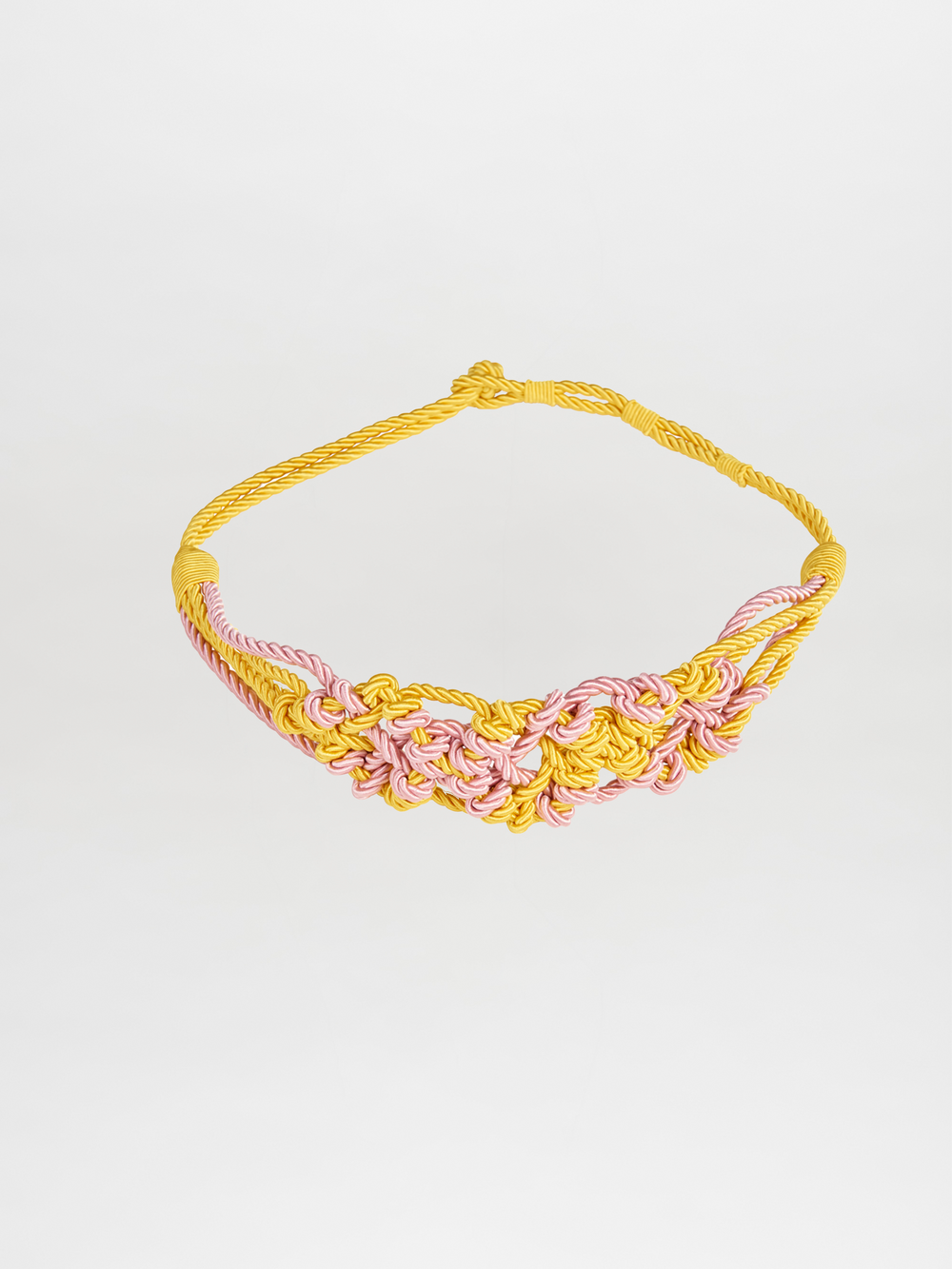 The Bresia Belt Yellow Pink, an intricately knotted braided necklace made of yellow and pink cords, is ready to ship. Displayed on a plain white background, it awaits your order.