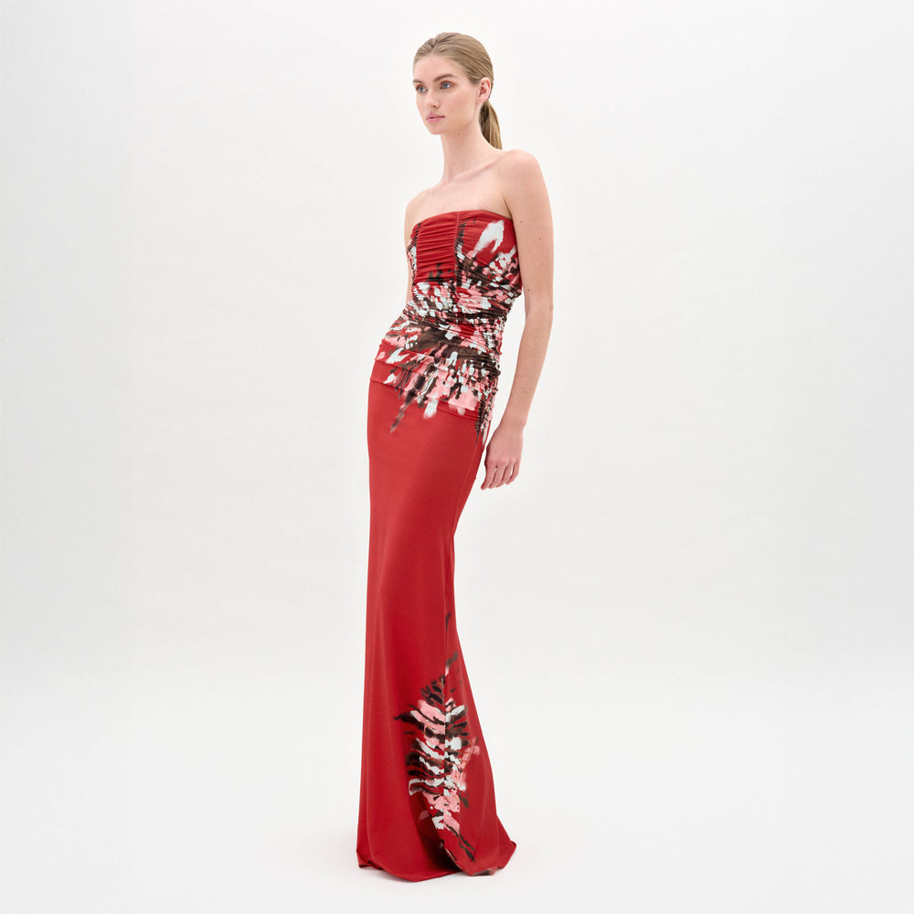 A woman wears the Collins Dress, a strapless maxi made from Italian fabric, with a fitted bodice and abstract white, pink, and black floral patterns on the skirt and waist.