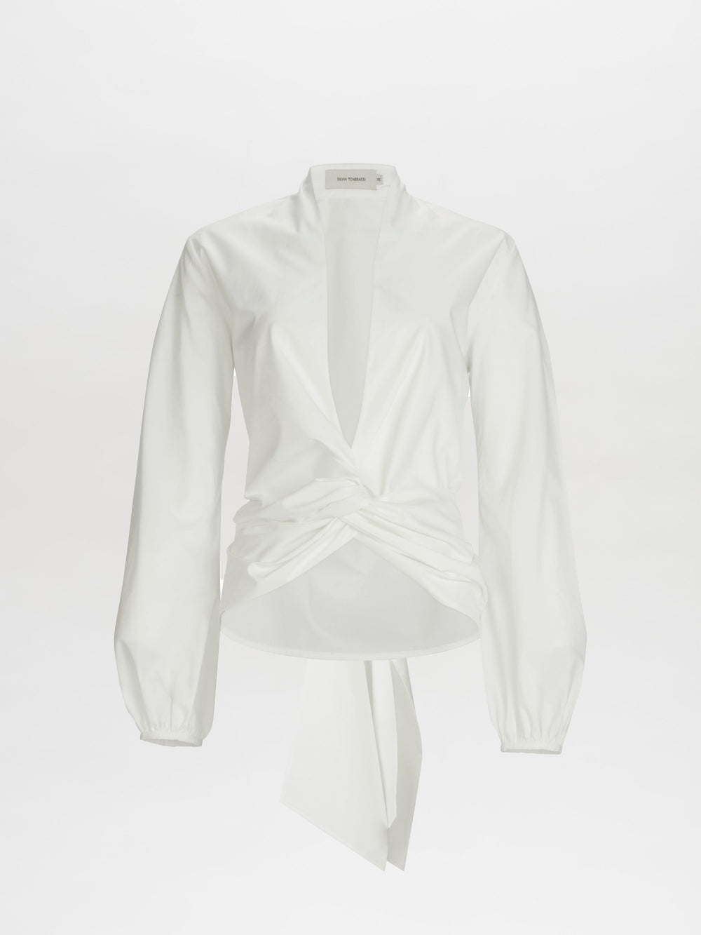 The Dania Blouse is a white long-sleeve top featuring a deep V-neck and twist knot detail at the front waist.