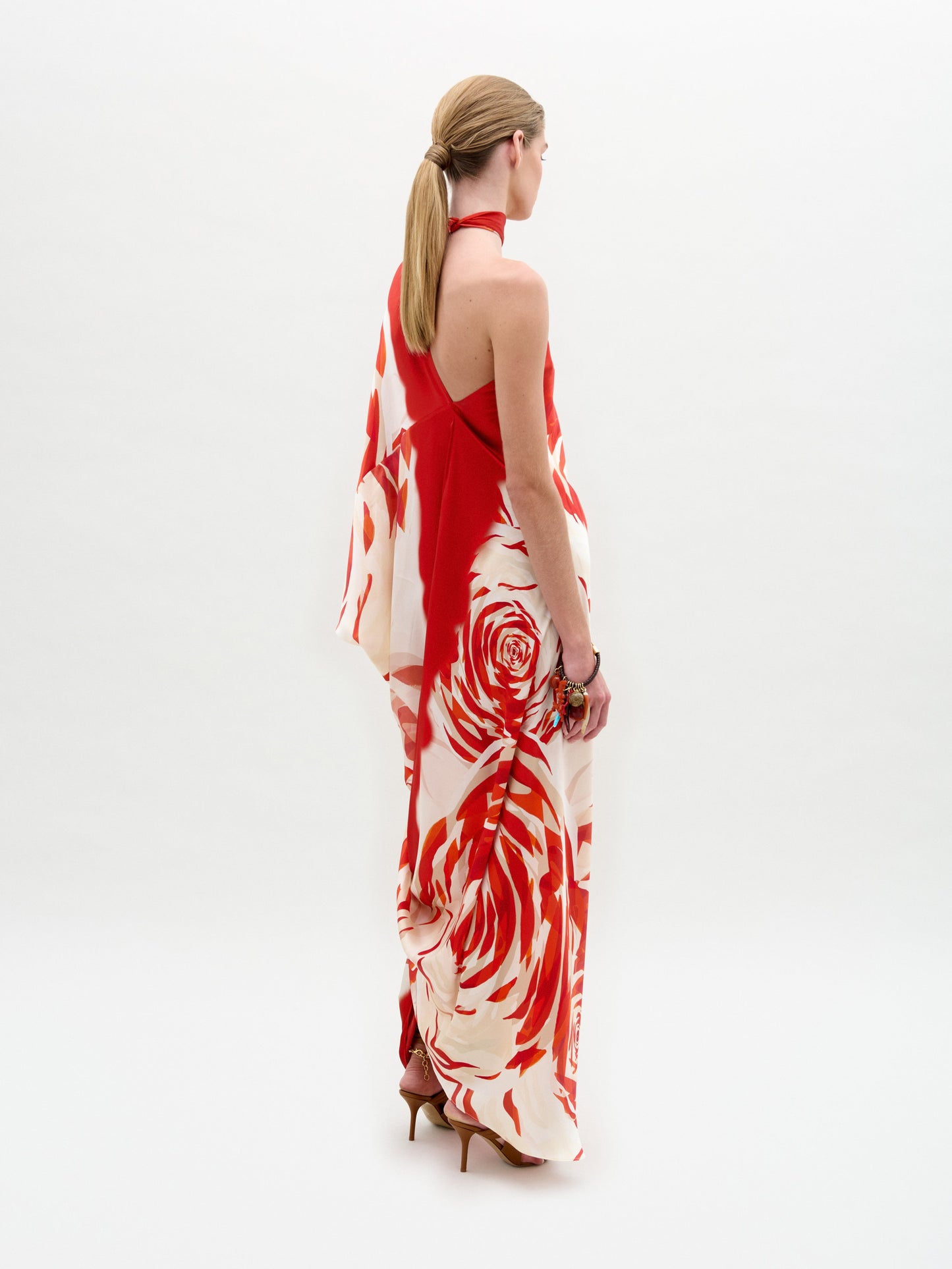 Woman standing in a Dani Tunic—red and white floral one-shoulder silk maxi dress with high heels and side slit—against a plain white background.
