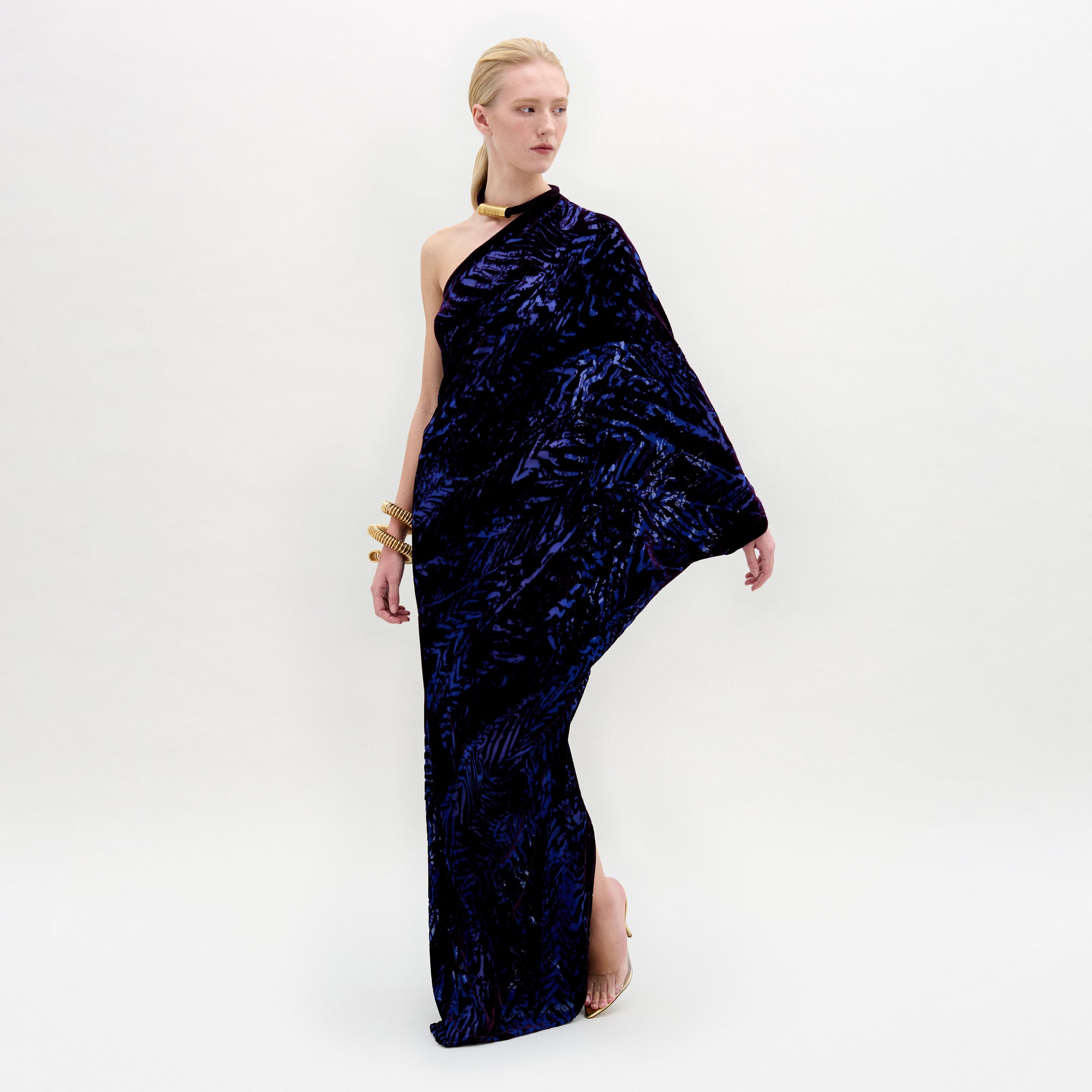 A person wearing the Erica Dress in color Eggplant Velvet with a golden necklace and bracelet on a white background.