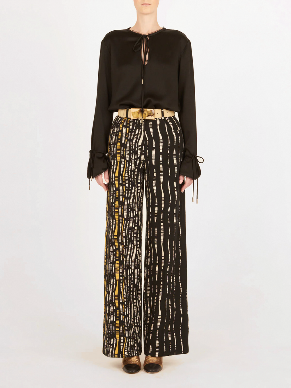Emine Pant Black White: High-waisted, wide-leg pants with a black base and white and yellow abstract line pattern, shown against a plain white background.