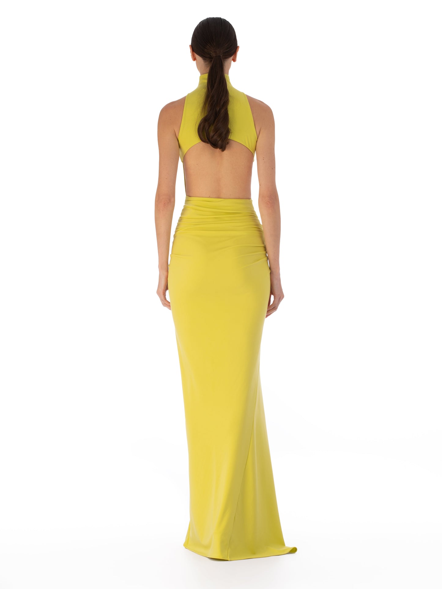 A person wearing the Frances Dress, a sleeveless, high-neck, floor-length yellow maxi dress with an asymmetric waistline and gathered detailing, stands against a plain white background.