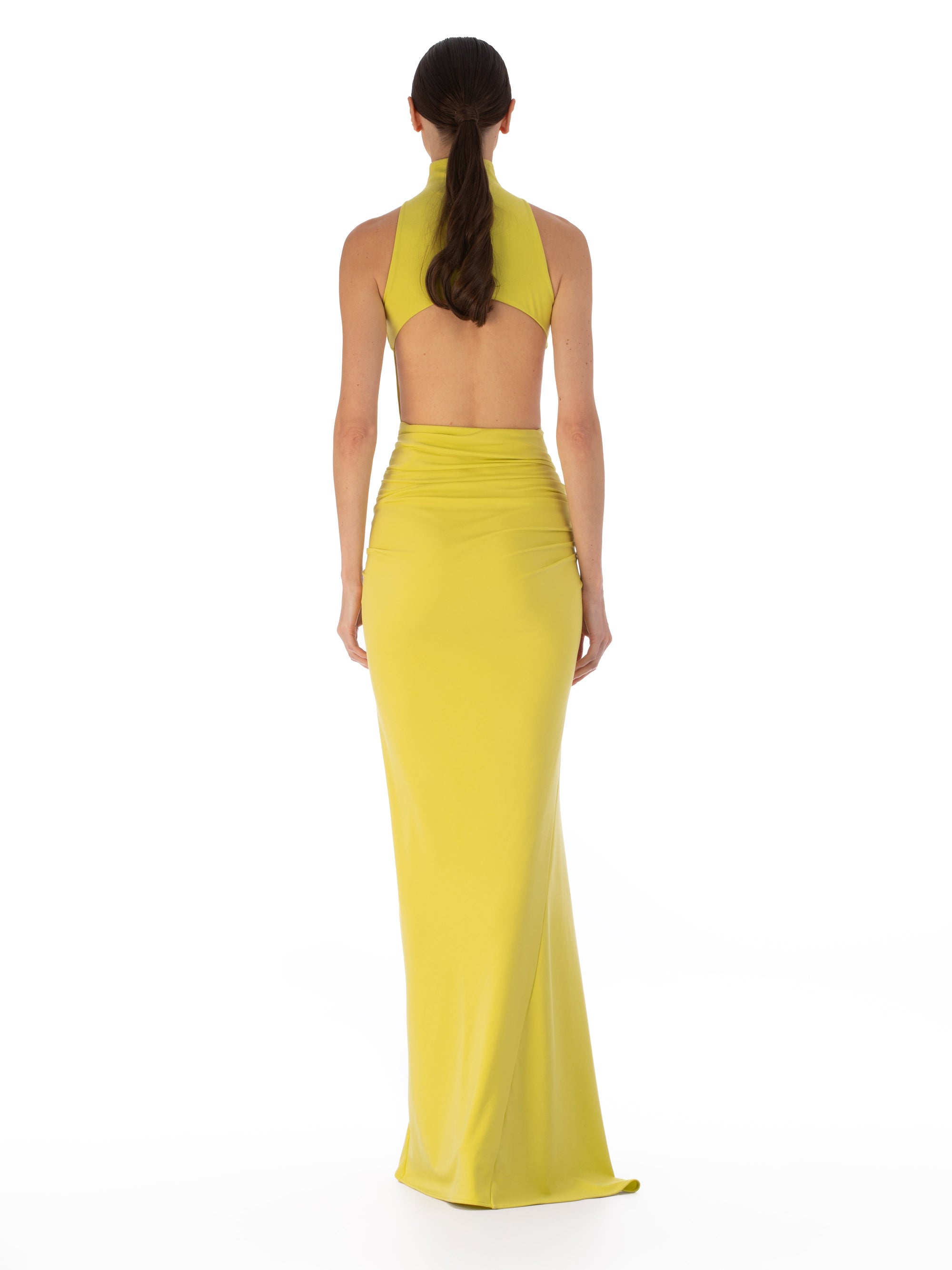 A person wearing the Frances Dress, a sleeveless, high-neck, floor-length yellow maxi dress with an asymmetric waistline and gathered detailing, stands against a plain white background.
