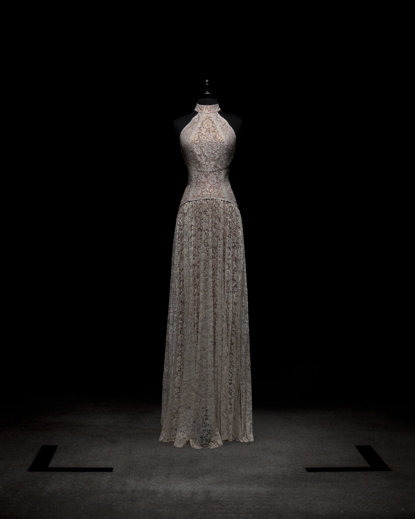 Wearing the Ilana Dress, a woman in a long lace bridal gown holds a bouquet of white and purple flowers against a plain background.