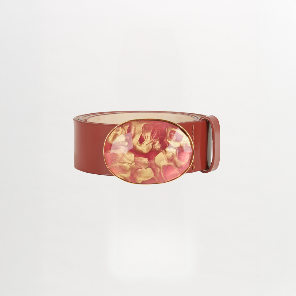 The Irene Belt Camel features glossy brown Italian leather, a wide strap, and a large oval resin buckle with a pink and gold marbled design. Shown on a white background, it's the standout accessory for Fall 2023.