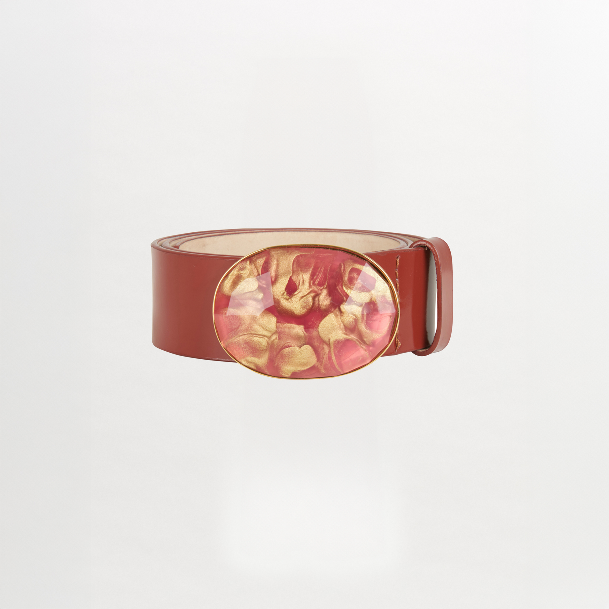 The Irene Belt Camel features glossy brown Italian leather, a wide strap, and a large oval resin buckle with a pink and gold marbled design. Shown on a white background, it's the standout accessory for Fall 2023.