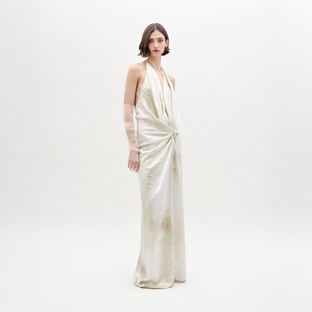 A woman wears the Jazmin Dress, a white, sleeveless halter gown, paired with semi-transparent gloves against a plain background.