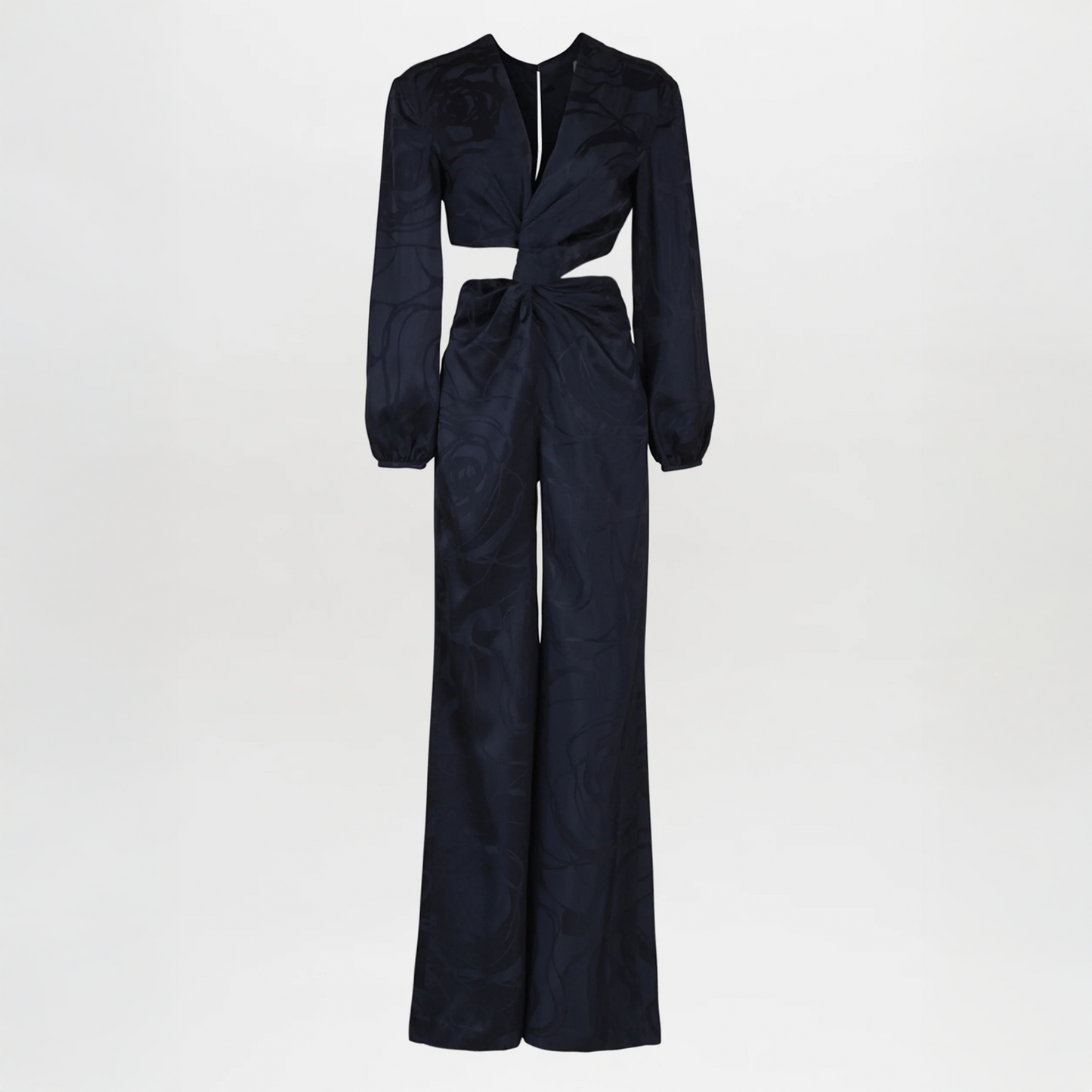 The Joely Jumpsuit Navy Jacquard, a black long-sleeve piece from the Resort 2023 collection, features a twisted front design, cutout at the waist, and wide-leg trousers.