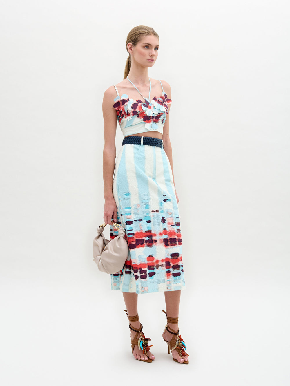 A person wears the Layan Skirt as a sleeveless patterned dress, paired with a beige bag and tassel-adorned strappy sandals.