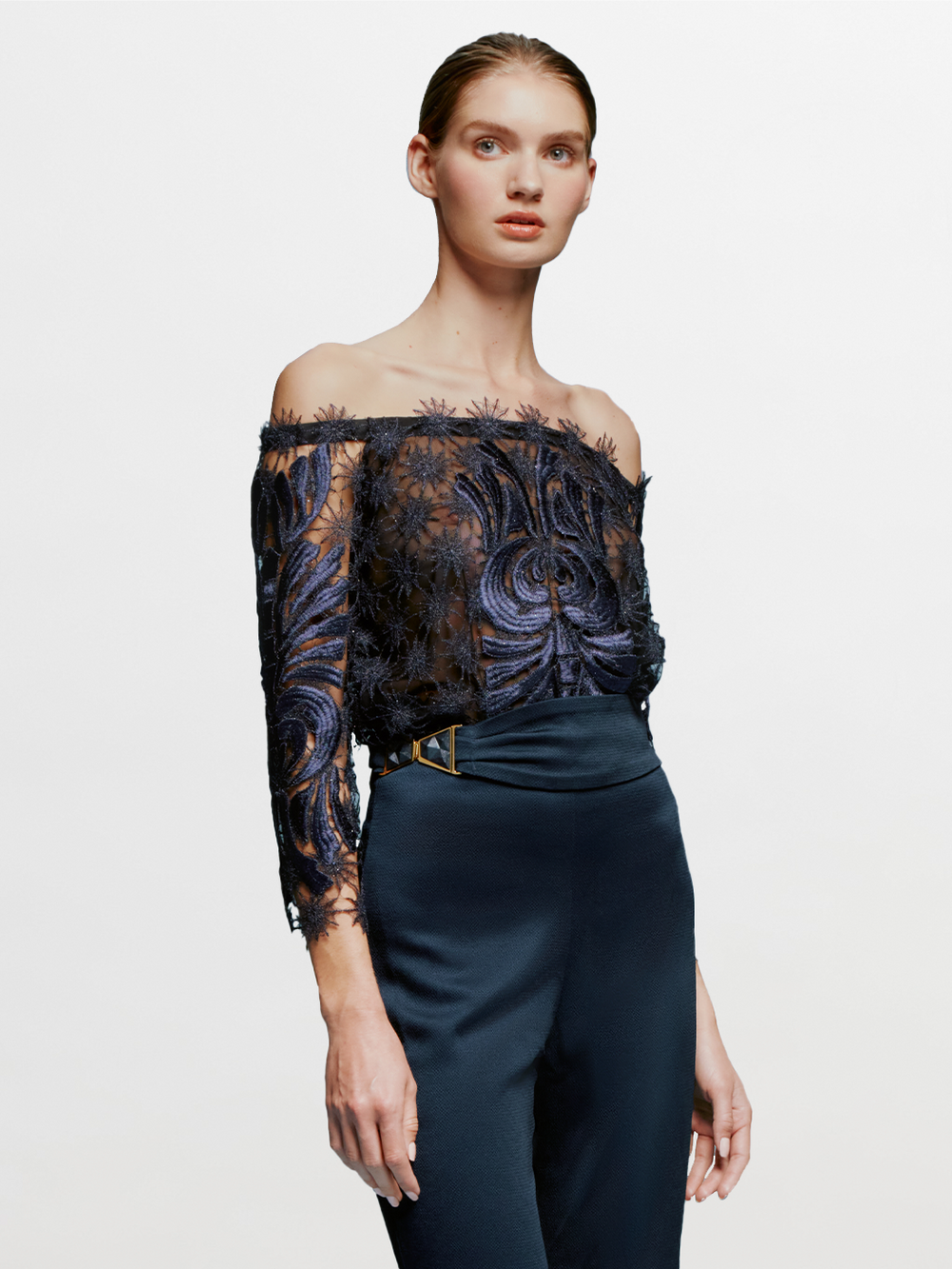 On August 19th, a person with slicked-back hair wears the Lala Blouse Navy with intricate patterns and high-waisted navy pants against a plain blue background.