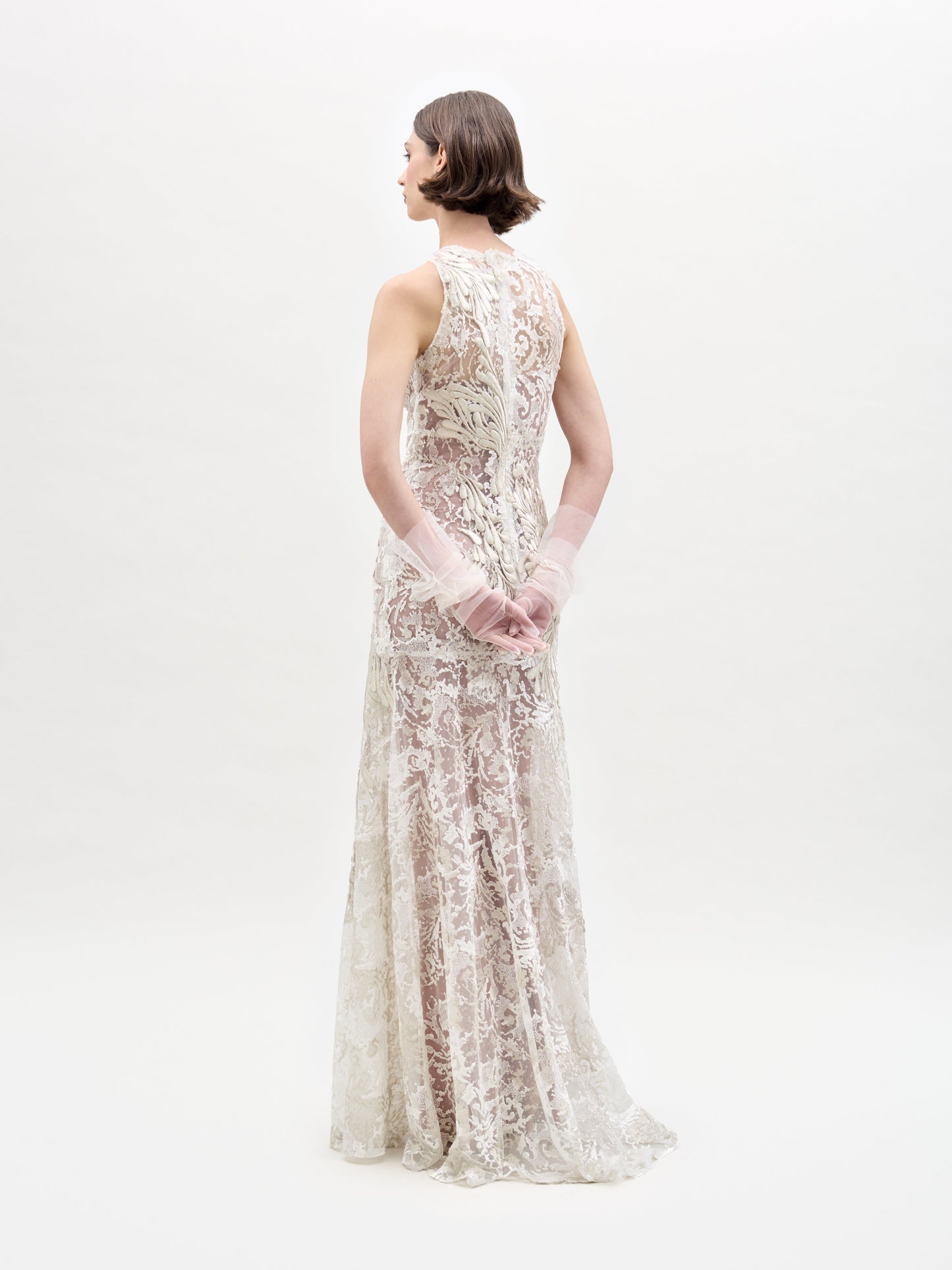 A woman models the Levi Dress, a sleeveless, floor-length maxi featuring floral embroidery and delicate appliqué, standing against a plain white background.