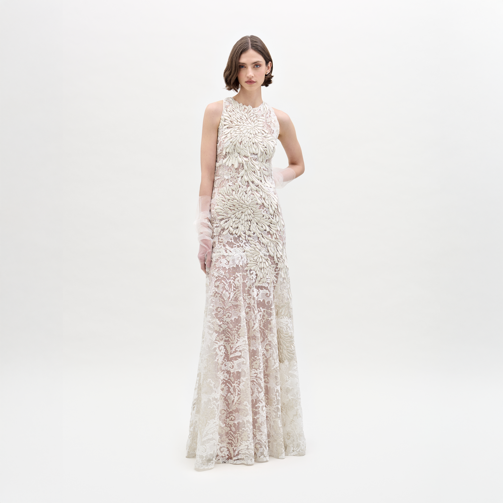 A woman models the Levi Dress, a sleeveless, floor-length maxi featuring floral embroidery and delicate appliqué, standing against a plain white background.