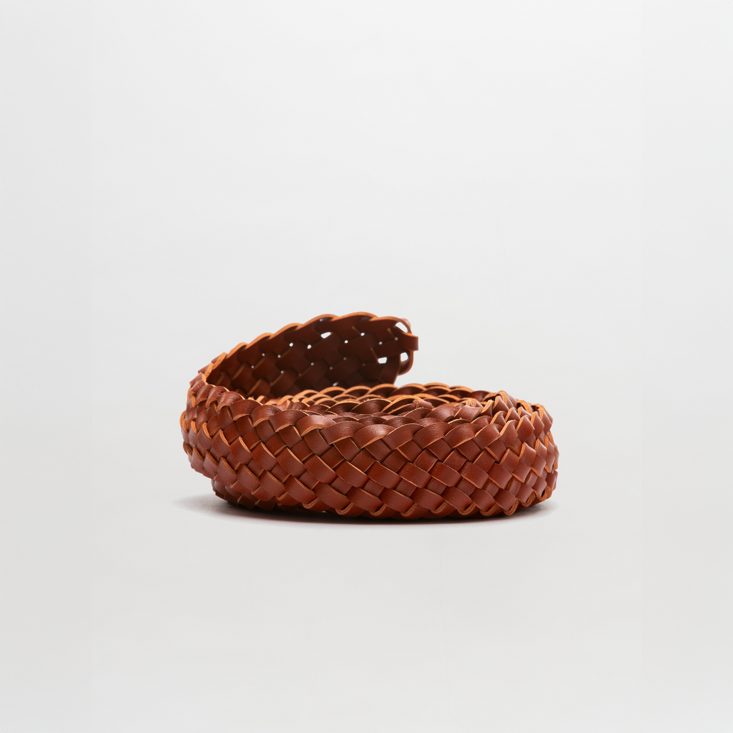 The Lauren Belt, a coiled brown braided accessory crafted from premium Italian leather, is displayed against a plain light grey background.