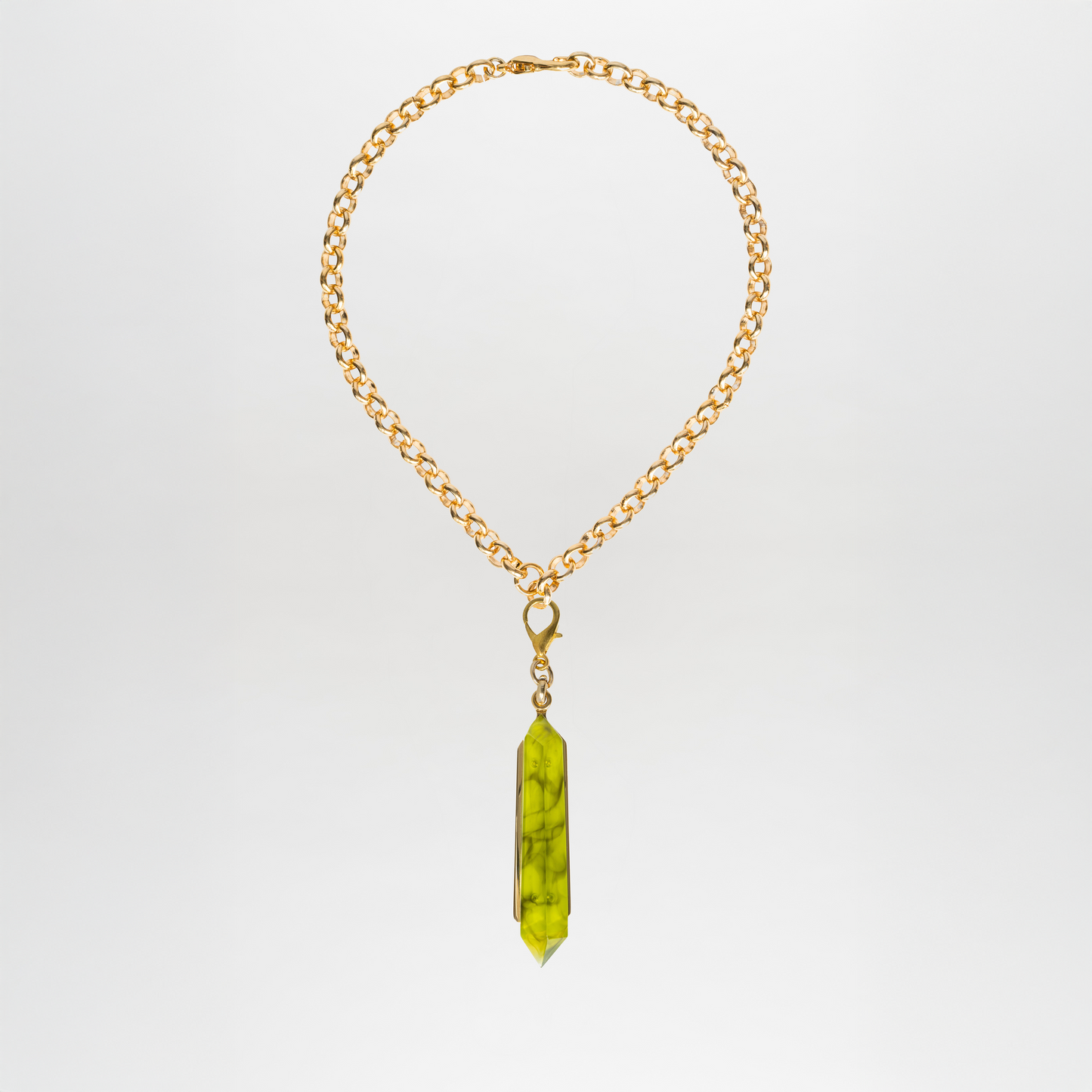 The Mariela Necklace is a striking gold-plated brass chain featuring a long, green crystal geometric pendant. This elegant piece adds sophistication and style to any outfit.