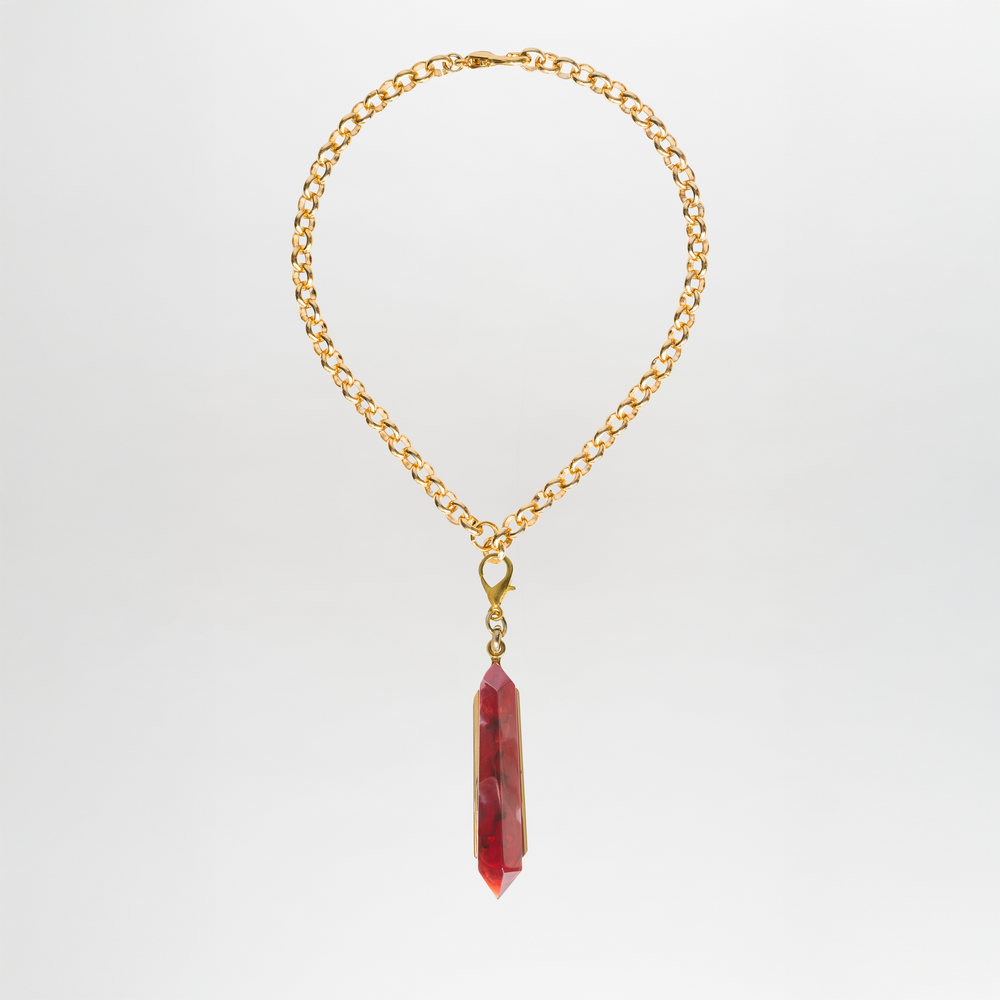 The Mariela Necklace is a gold-plated brass choker featuring a single geometric red crystal pendant, showcased against a plain white background.