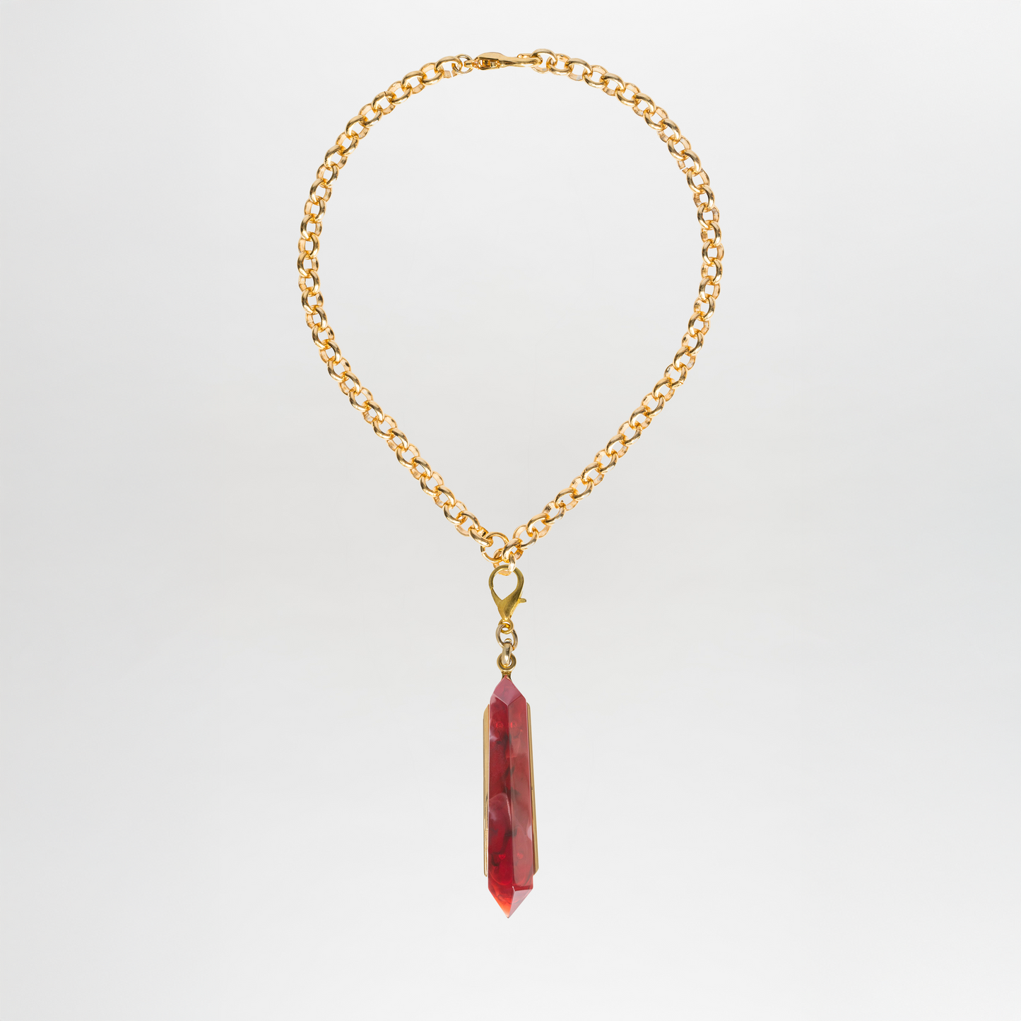 The Mariela Necklace is a gold-plated brass choker featuring a single geometric red crystal pendant, showcased against a plain white background.