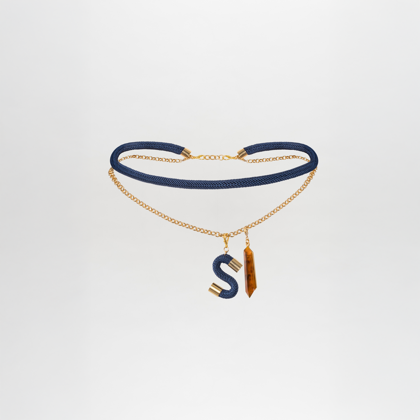 The Mireya Belt features gold chain links with blue accents, a gold and blue letter S pendant, and a long, gold-capped brown stone, shown on a plain white background.
