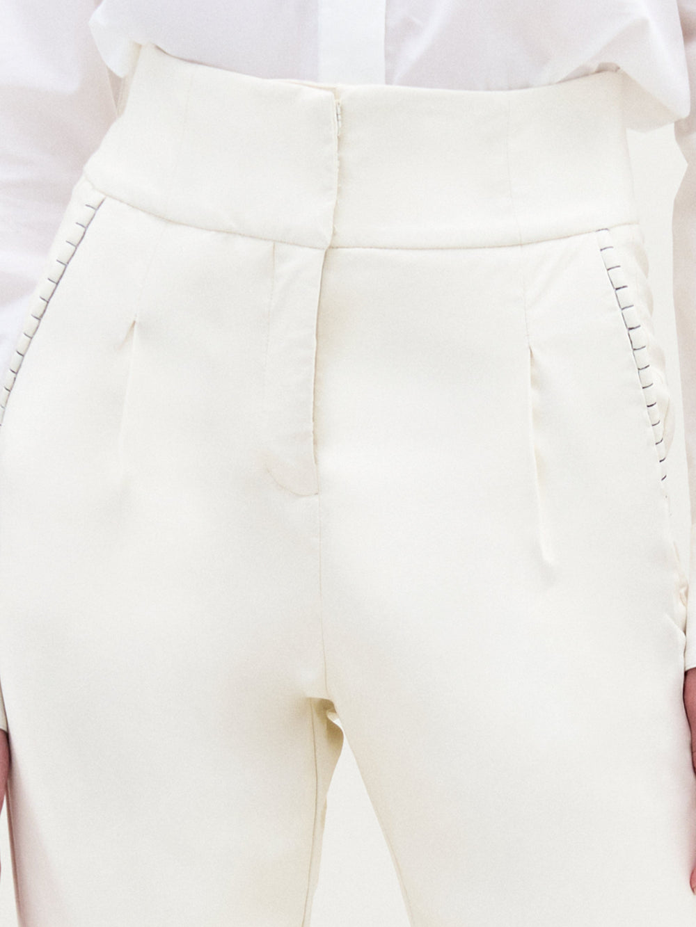 A person stands against a plain light background, wearing a textured white sweater, white collared shirt, the Moad Pant—an Italian fabric high-waisted cropped pant—and white heeled boots.