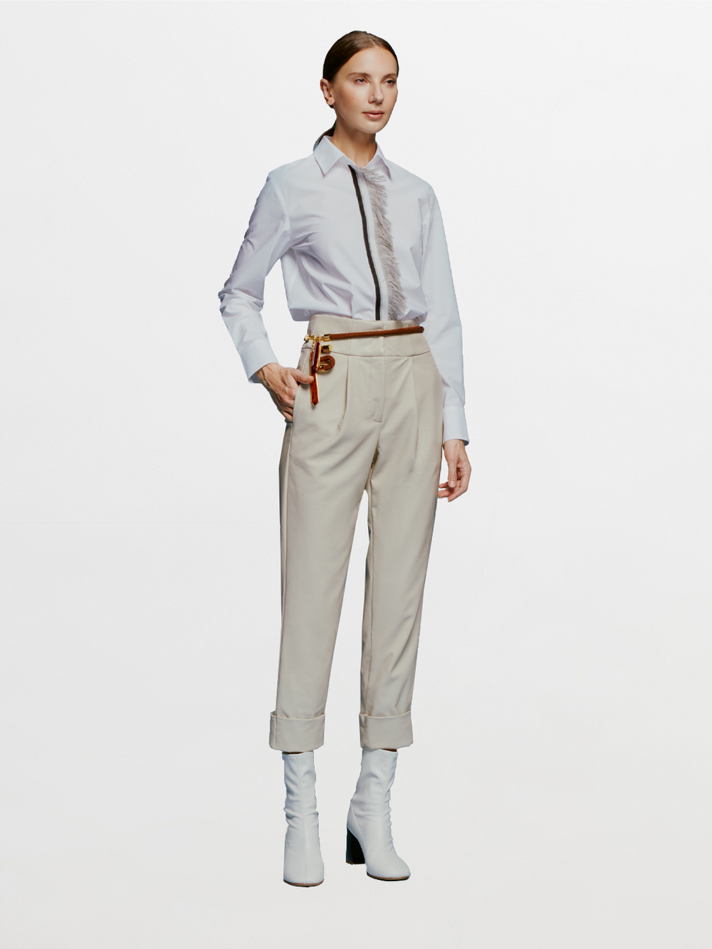 A person stands against a blue background, wearing a white shirt, black tie, Moad Pant Cream high-waisted pants, a brown belt with a keychain dated September 2nd, and white heeled boots.