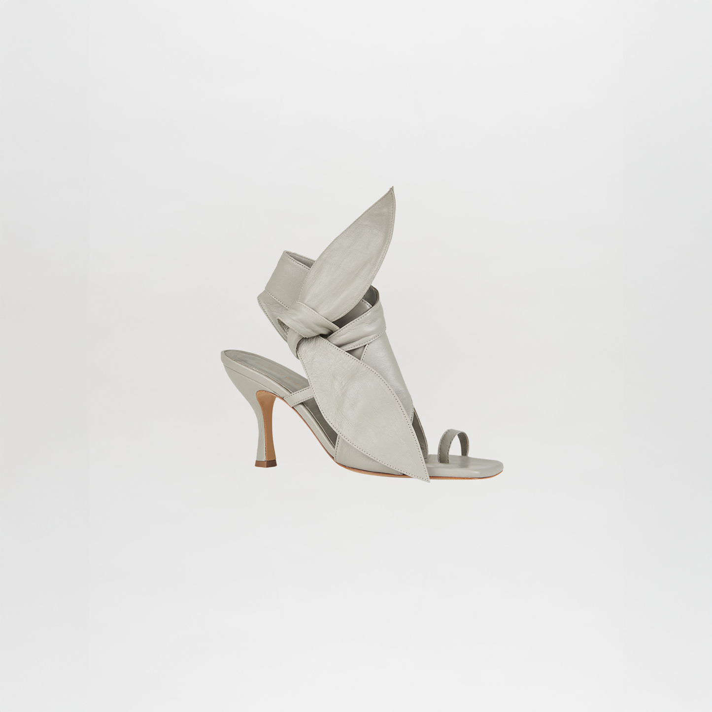 The Marco Heel Light Grey is a high-heeled sandal in Italian calf leather with a pointed sculptural bow and open toe, displayed on a white background.