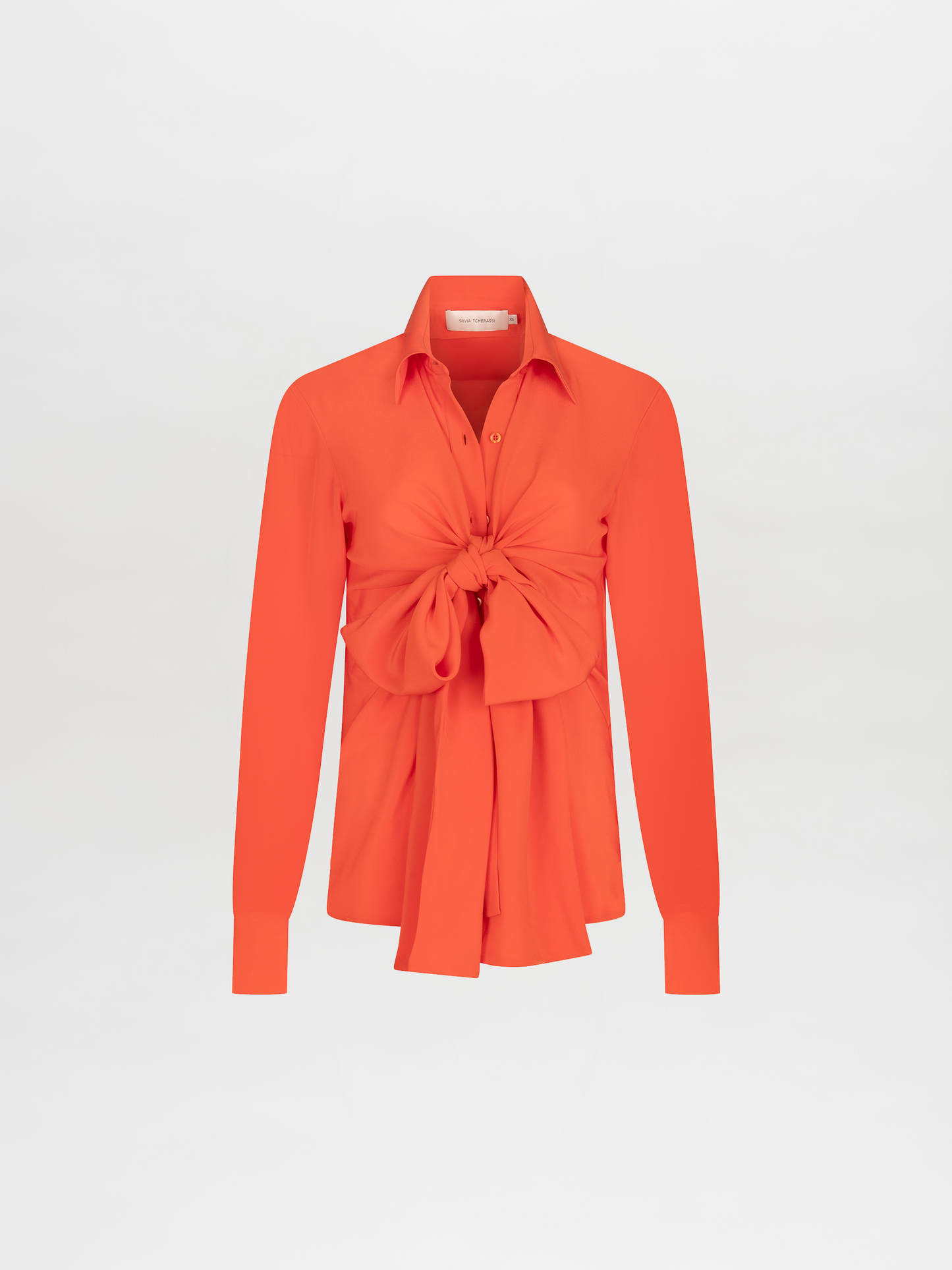 The Mercury Blouse Tangerine is a vibrant orange silk top with long sleeves, a collar, button-down front, and an oversized front knot at the waist, shown on a plain white background.