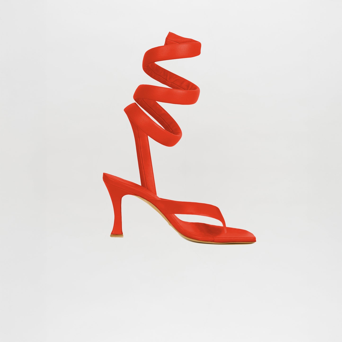 The Mika Heels Red are bright red high-heeled sandals made from Italian calf leather, featuring a spiral ankle strap, showcased on a plain white background.