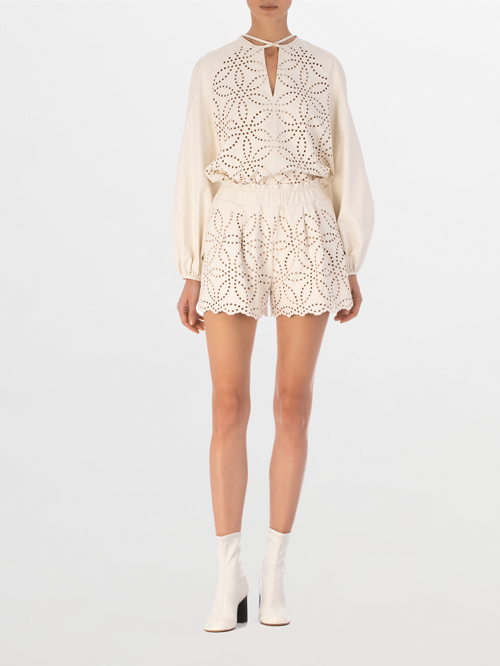 The Molveno Blouse Pearl is a white long-sleeve ecoleather blouse, featuring a geometric pattern on the front, a keyhole neckline, and a rounded hem.