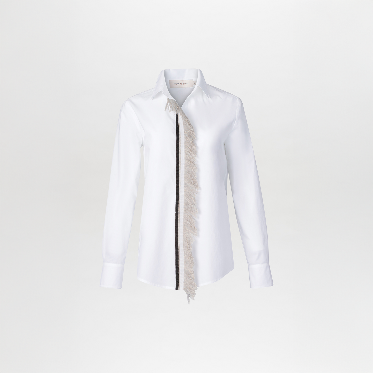 The Naroa Blouse is a white long-sleeve cotton blouse with a classic shirt collar, raw lace fringe detailing along the left front placket, and tailored cuffs for a refined touch.