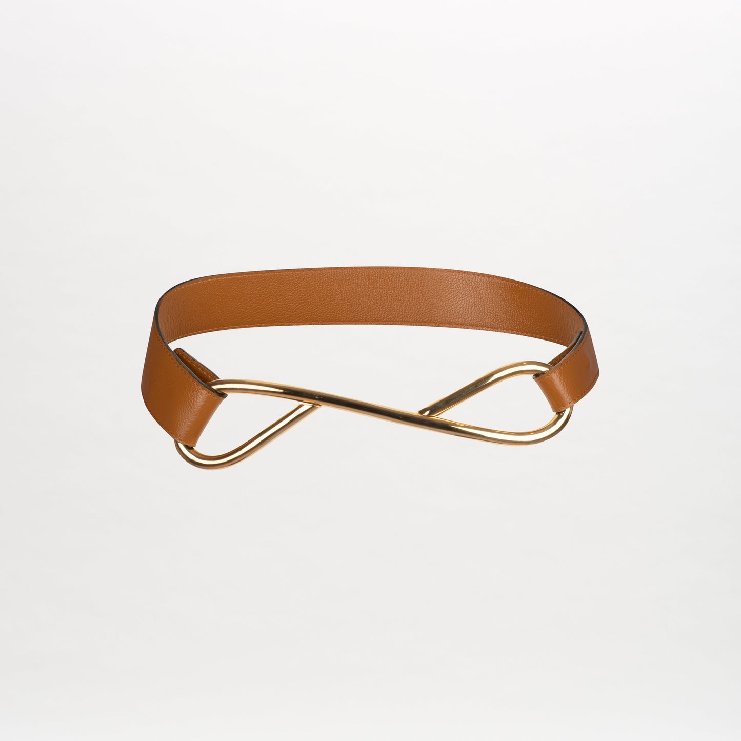 The Odelia Belt, crafted from brown leather in Colombia, showcases a striking gold-tone abstract twisted metal buckle, set against a plain white background.