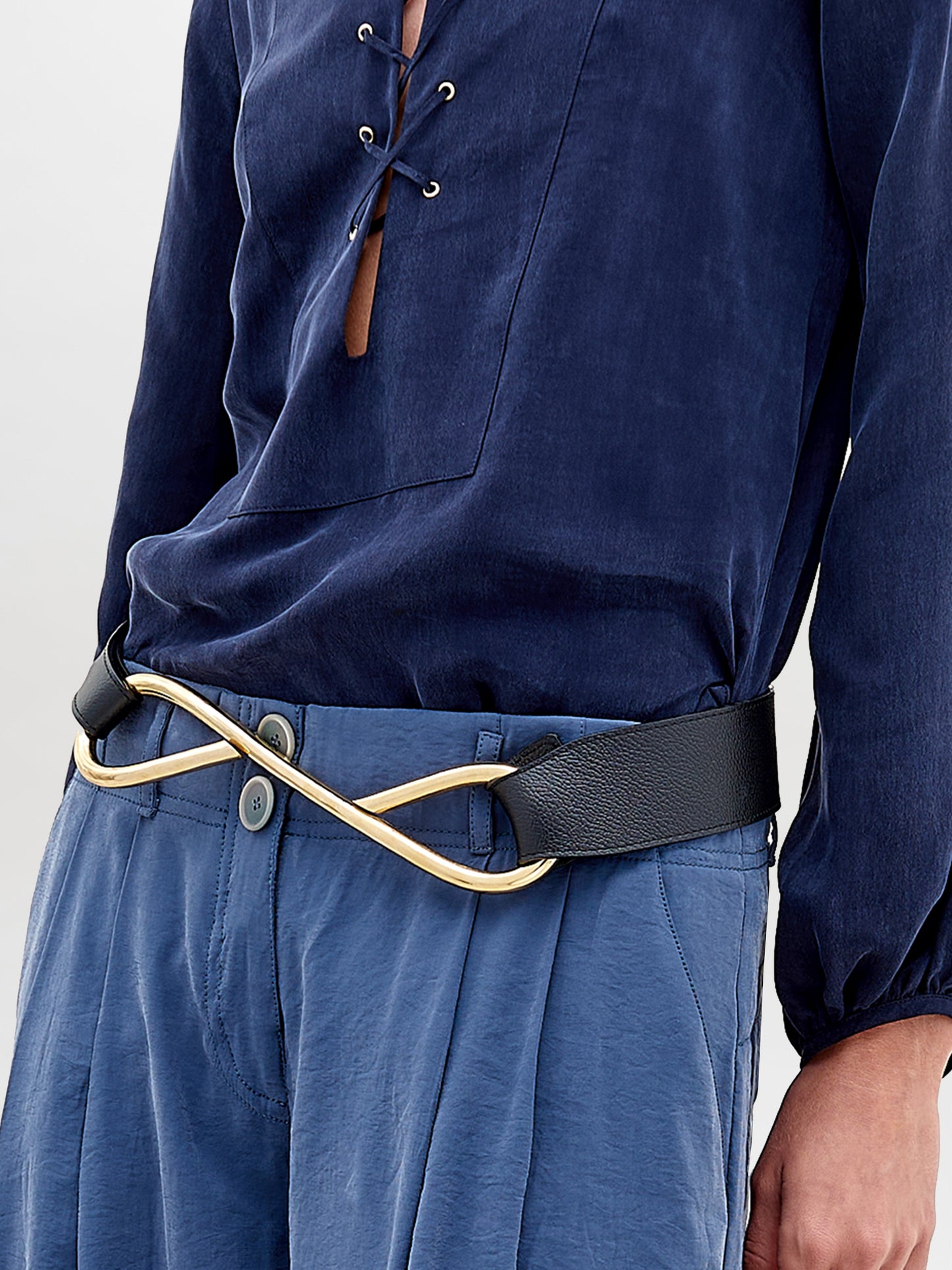 The Odelia Belt is a sleek black leather accessory with a gold-tone buckle, featuring a seamless loop design against a plain white background.