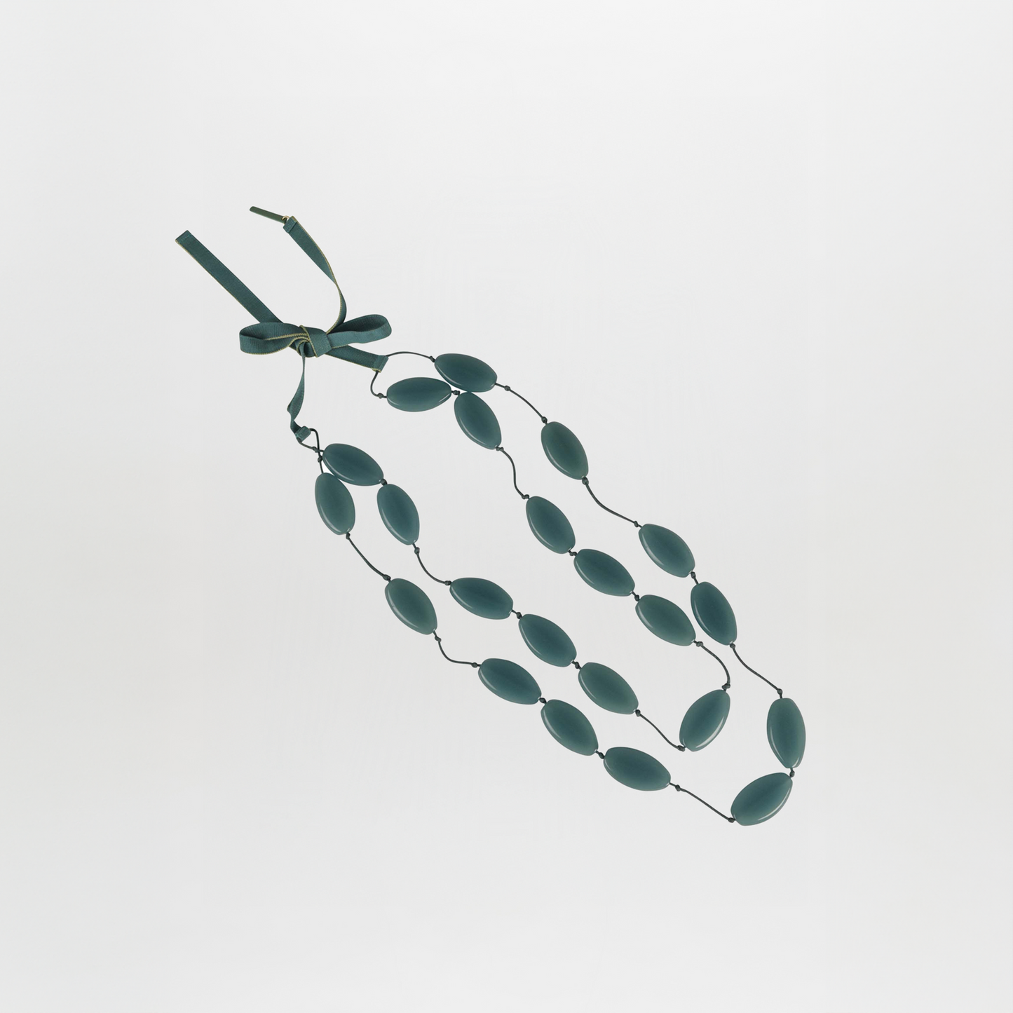 The Olivia Necklace Emerald features three strands of oval teal Italian resin beads on thin cords, finished with a matching ribbon tie.
