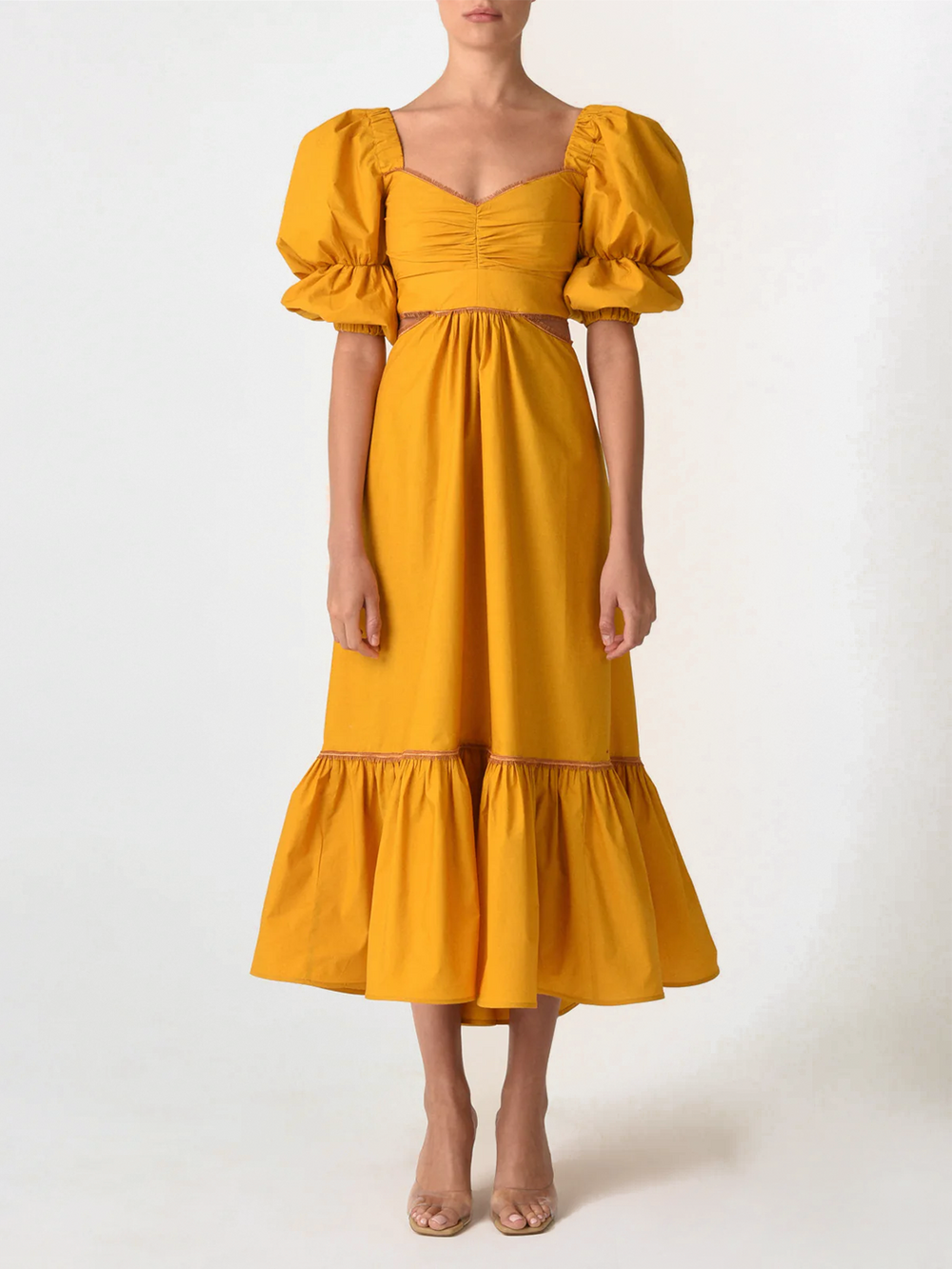 Introducing the Peggie Dress Marigold, a stunning Silvia Tcherassi dress in mustard yellow, featuring puffed sleeves, a fitted bodice, side cutouts, and a ruffled hem—an essential piece from Resort 2023.