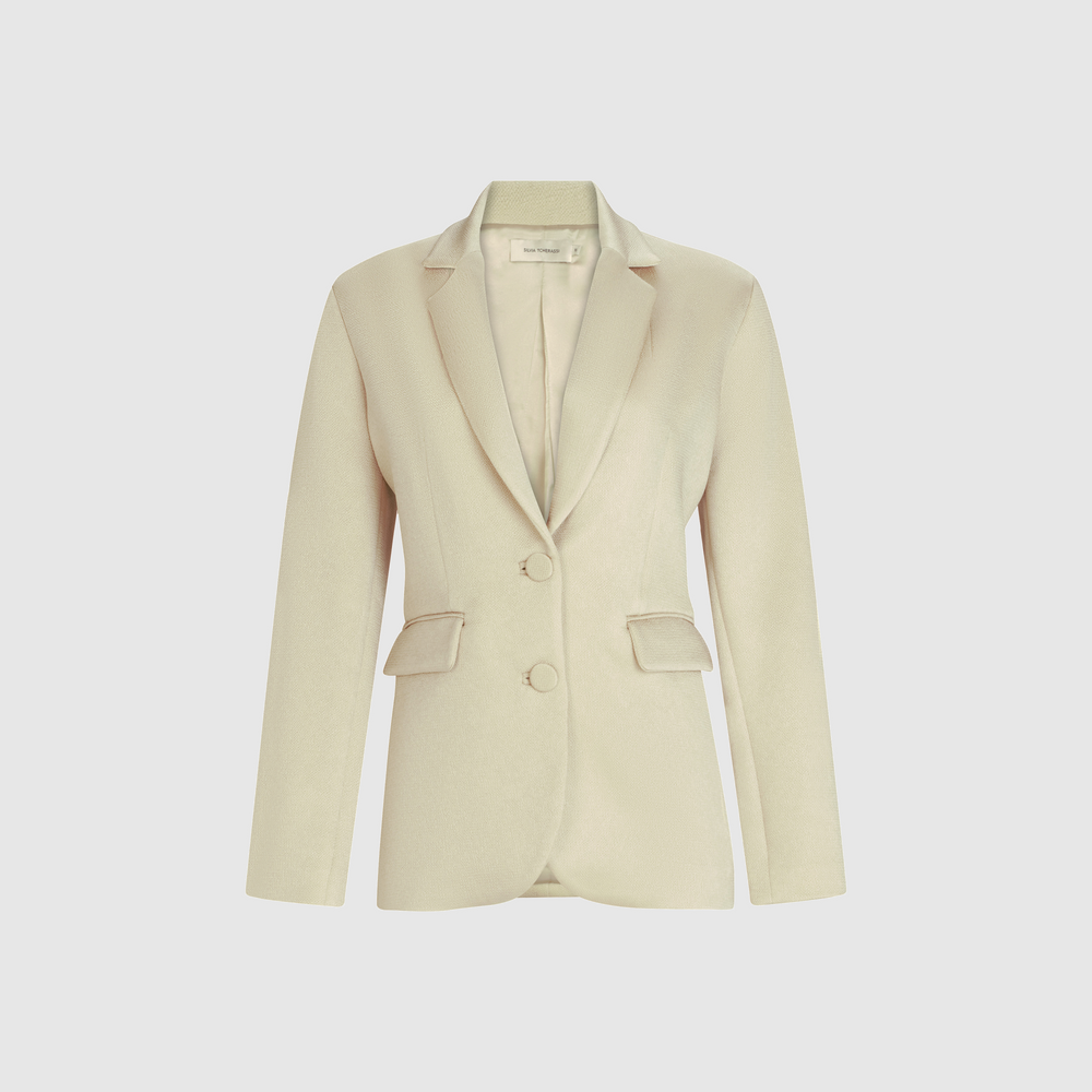 The Rebeca Jacket is a beige women's blazer made from Italian fabric, featuring notched lapels, a structured silhouette, two front buttons, and flap pockets, shown against a plain white background.