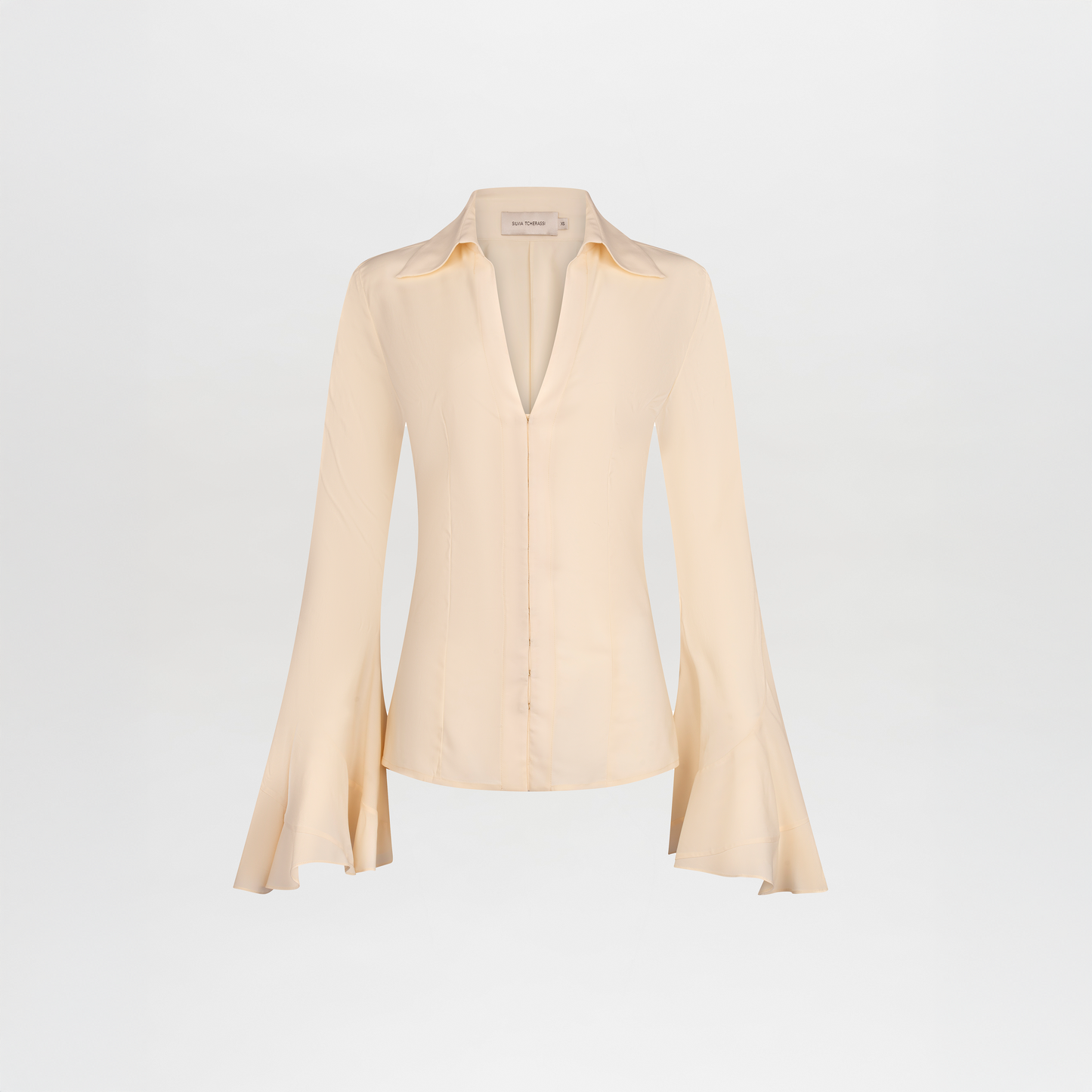 The Reggie Blouse is a light beige silk top with long sleeves, a deep V-neck, and elegant flared bell sleeves, shown against a plain white background.