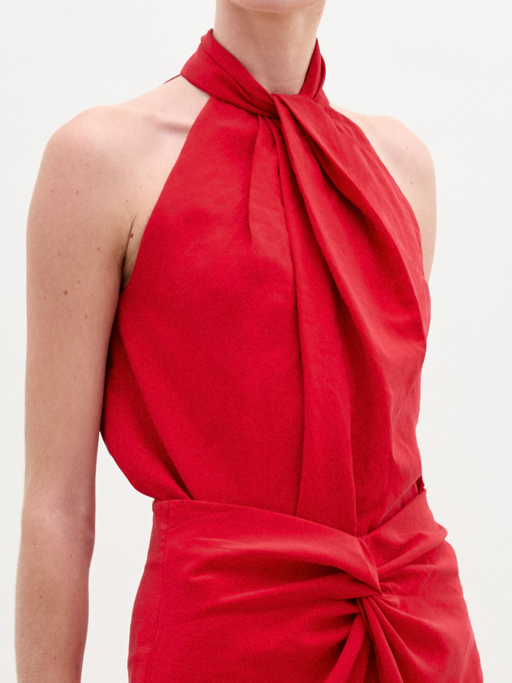 Person wearing the Shela Blouse, a relaxed fit, sleeveless, high-neck red top with a knotted waist detail, standing against a plain white background.