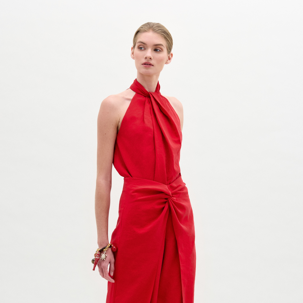 Person wearing the Shela Blouse, a relaxed fit, sleeveless, high-neck red top with a knotted waist detail, standing against a plain white background.