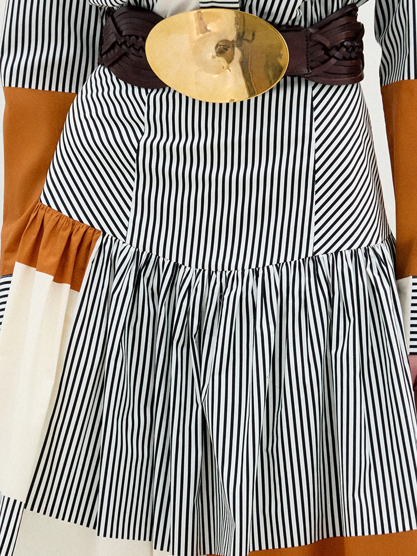 Black and white striped dress with a brown belt and gold buckle on a wooden surface.